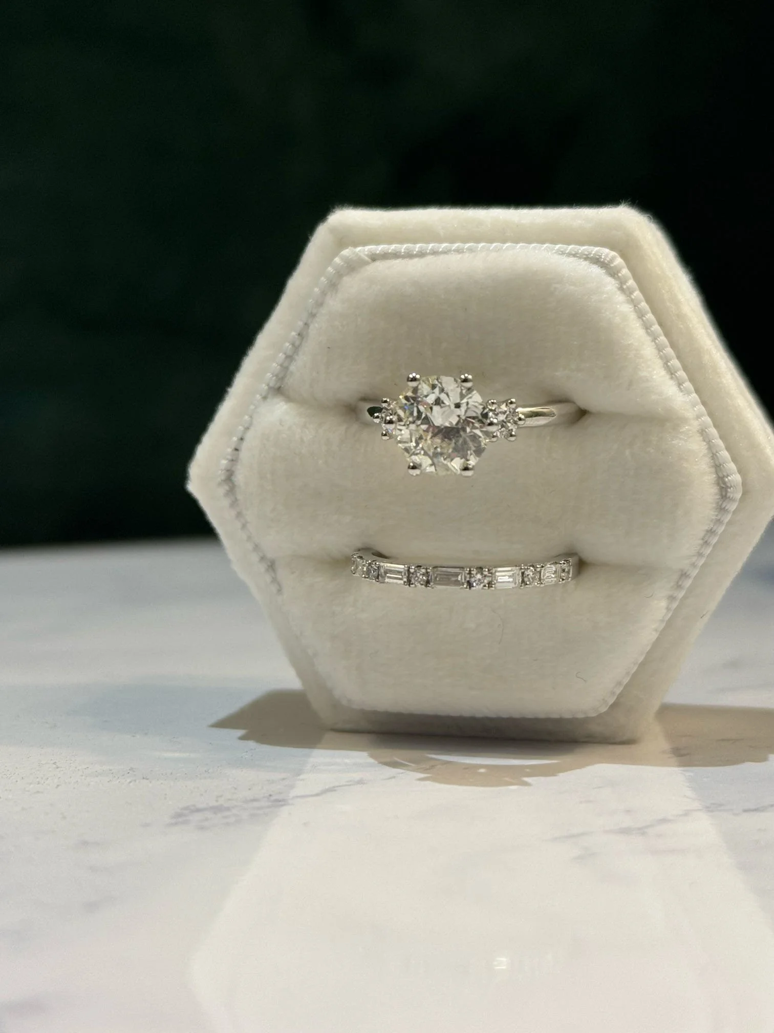 Two diamond rings displayed on a white ring box, with a dark background.