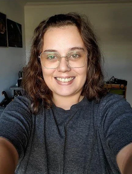 Une femme souriante portant des lunettes, prenant une selfie dans une pièce domestique.