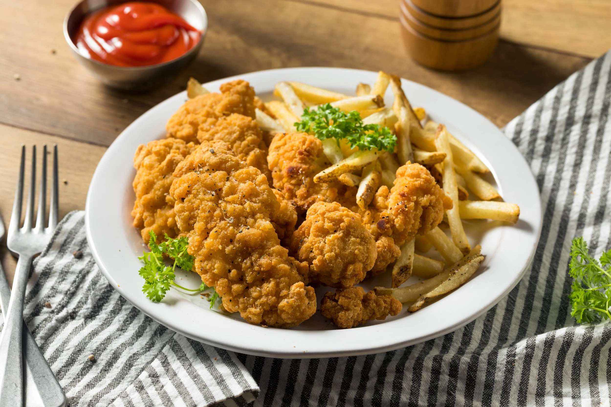 Plate of fried chicken tenders and fries with ketchup.