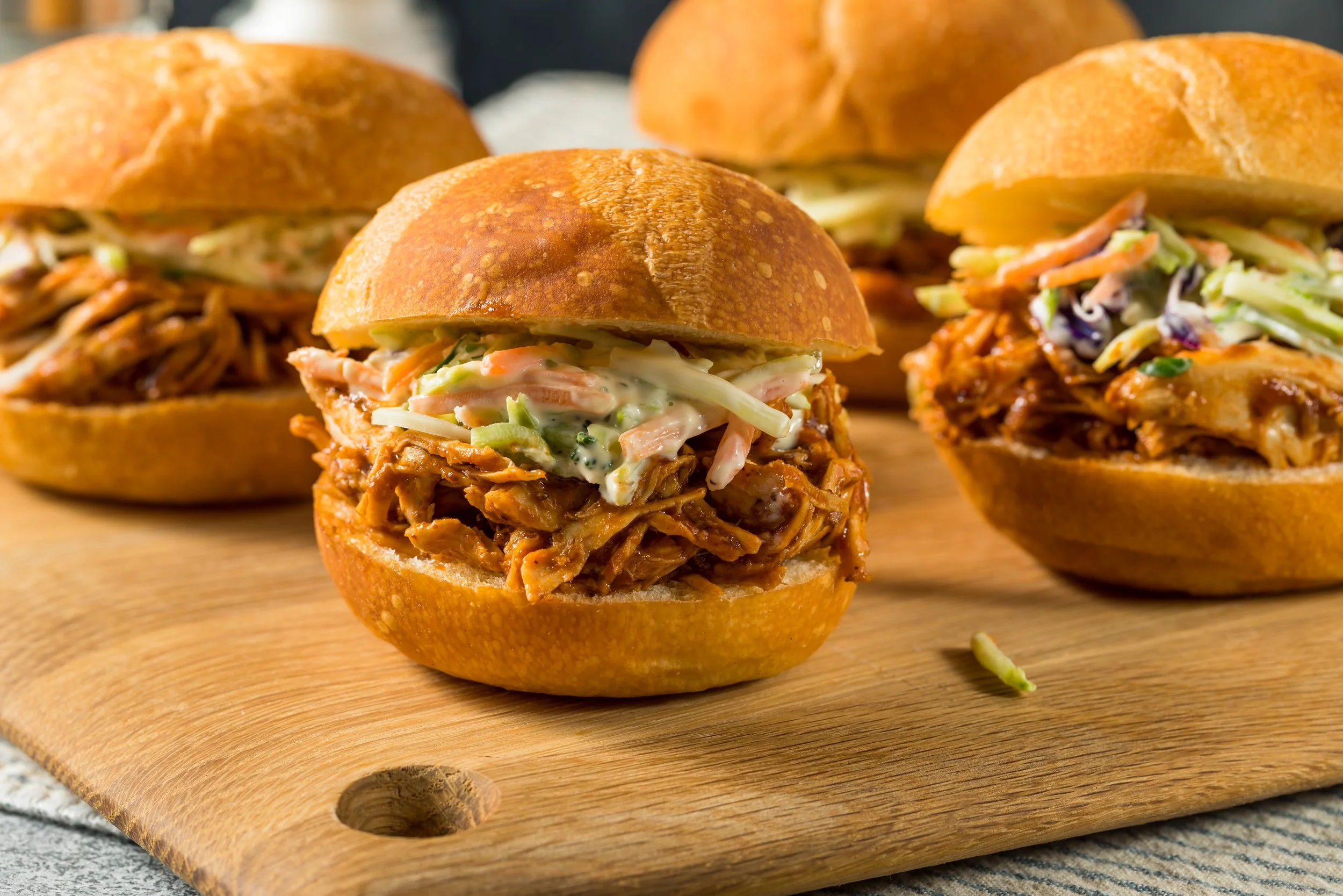 Barbecue pulled chicken sandwiches with coleslaw on wooden board.