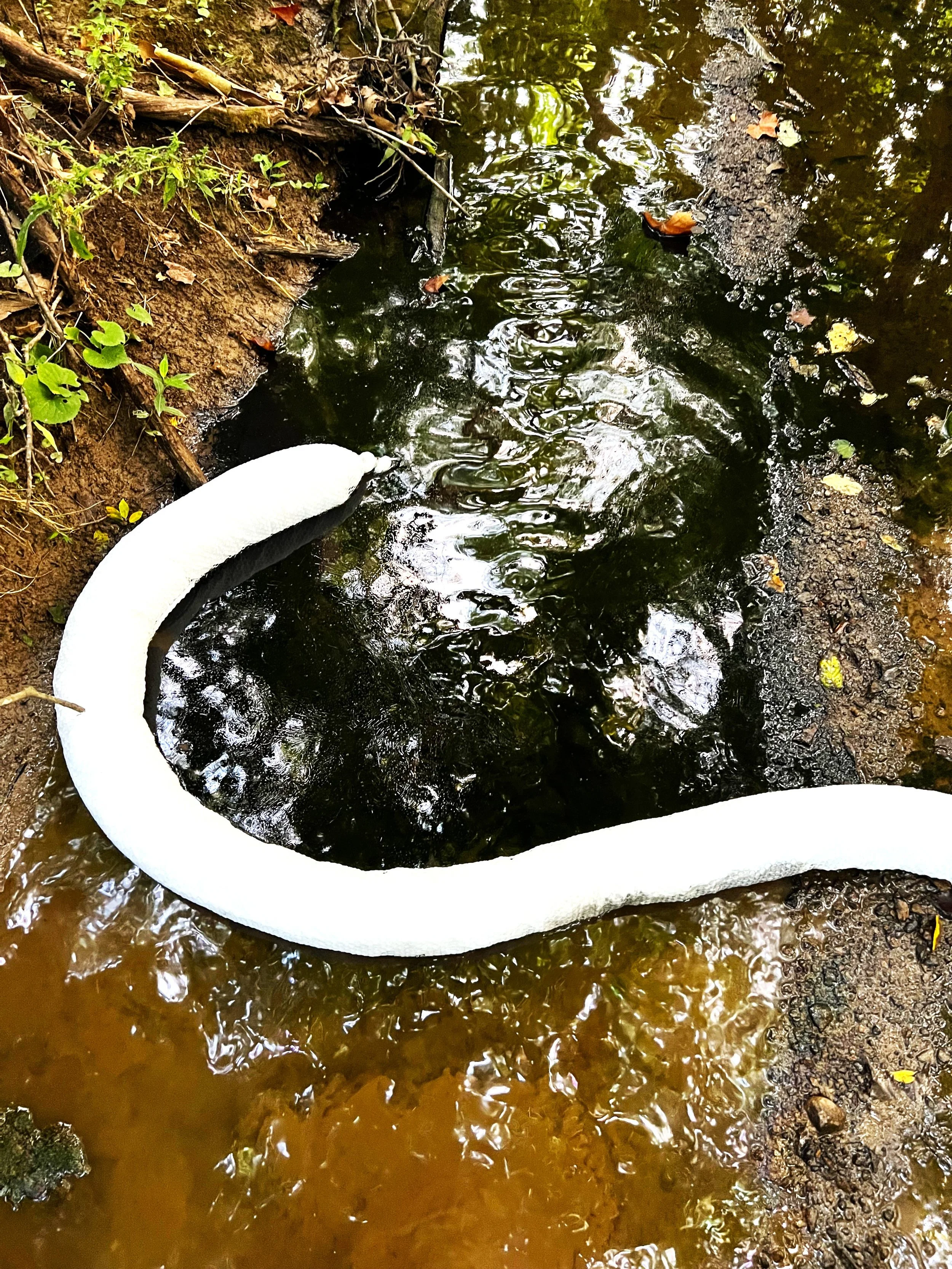 Emergency containment measures deployed to control petroleum contamination within an impacted creek system. Absorbent booms were strategically positioned to capture free product, limit downstream migration, and support environmental recovery efforts 