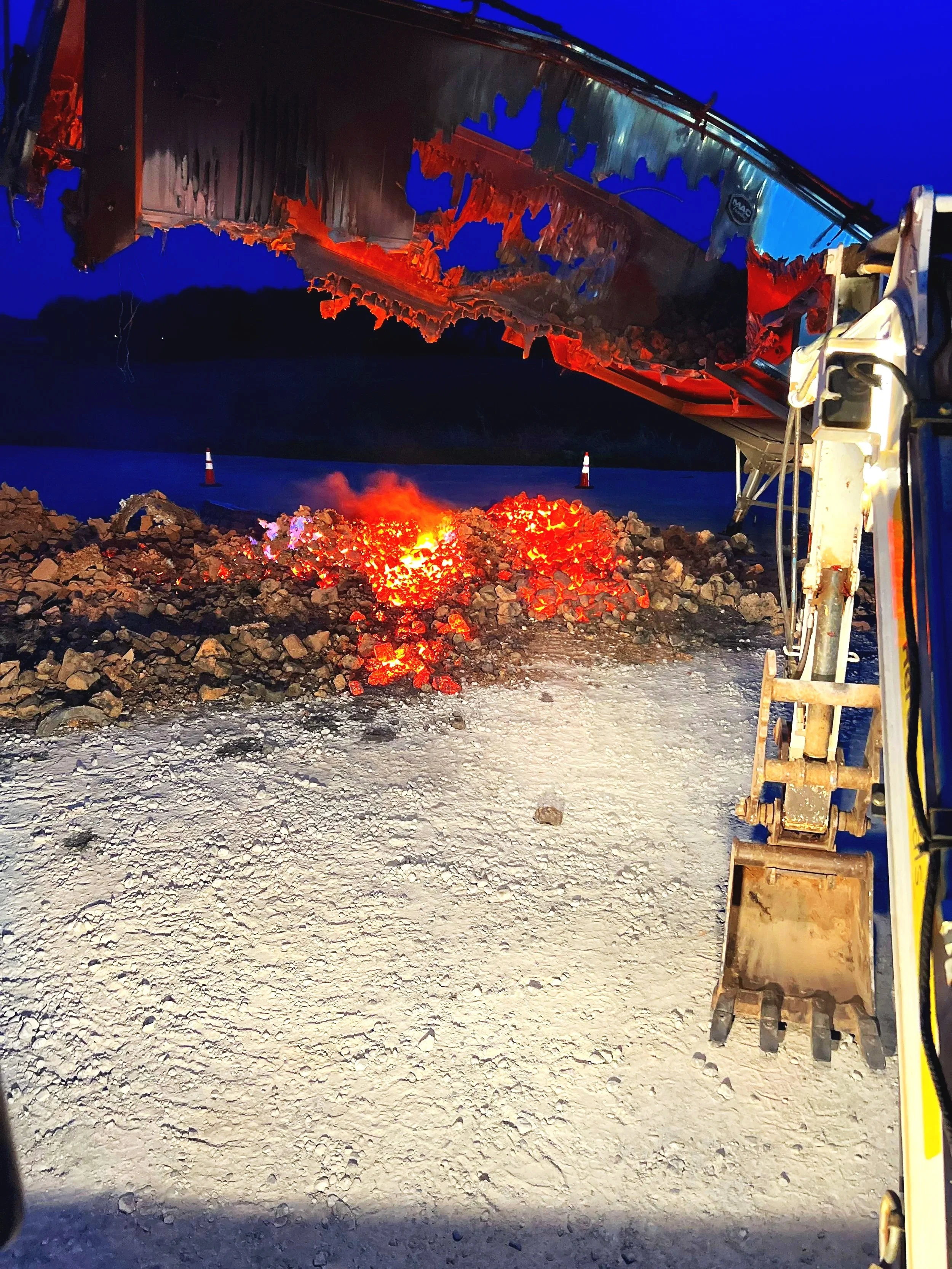 Hot material and smoldering debris being removed after a commercial trailer fire during emergency response.