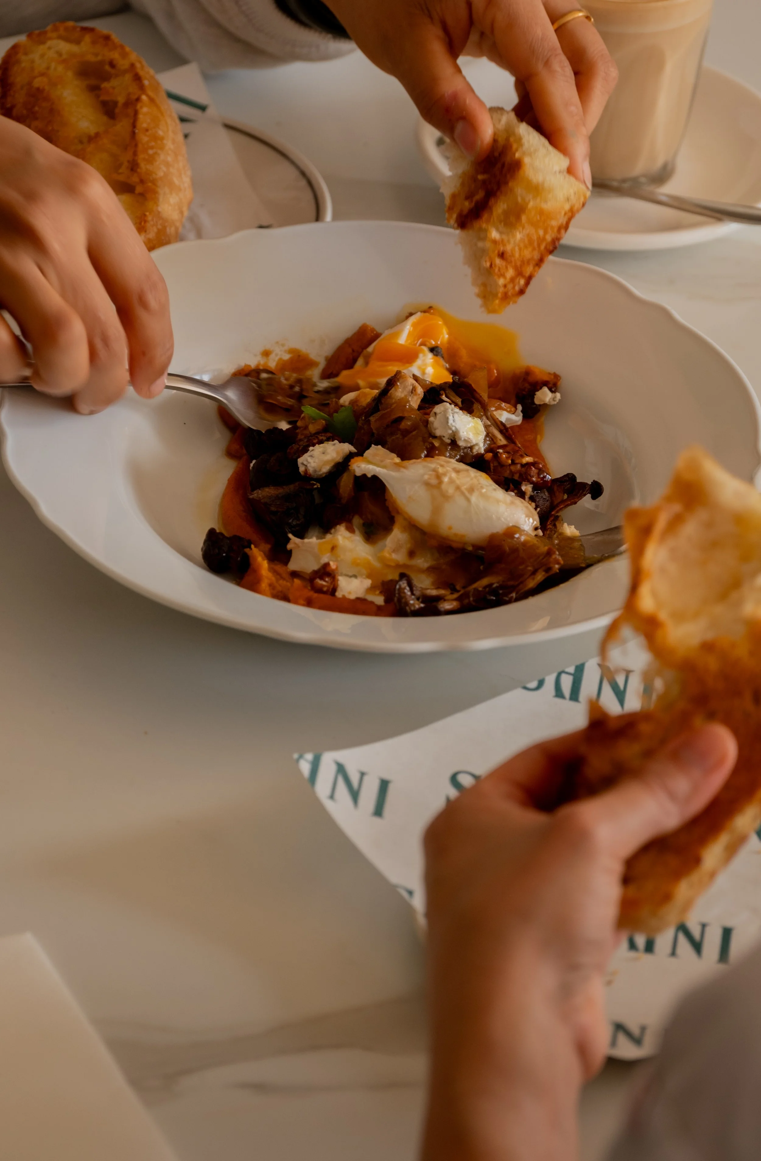 Hands holding pieces of bread and a bowl of eggs with black beans and cheese.