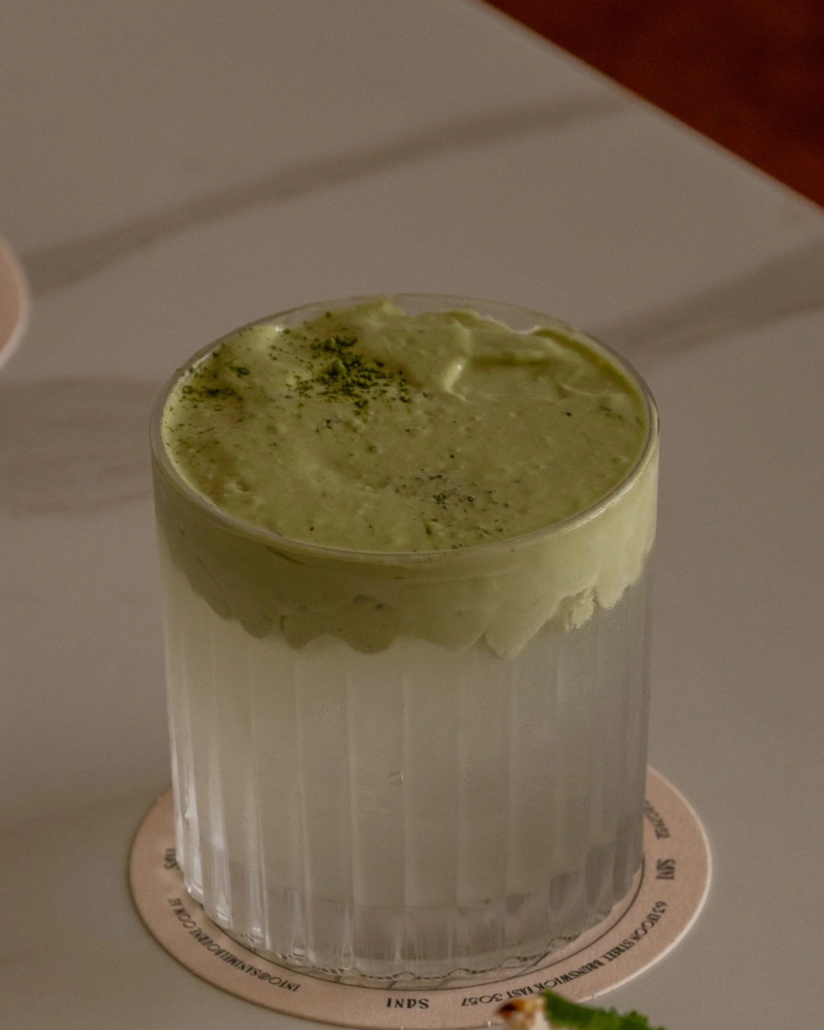 A glass of matcha latte topped with green powder on a white surface.