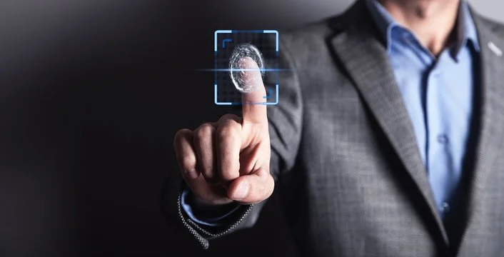 A person in a gray suit and blue shirt touching a virtual fingerprint scanner in a dark environment.