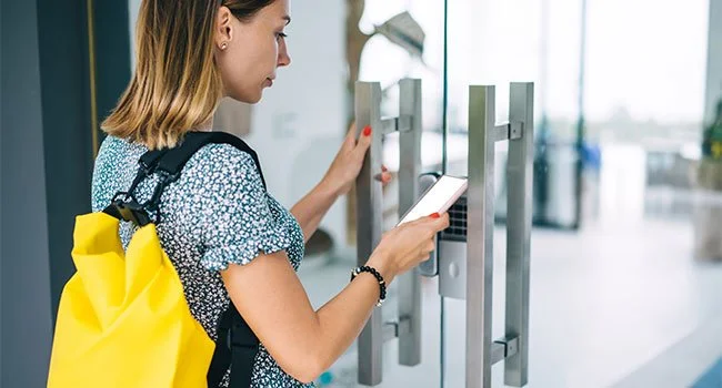Young woman with a yellow backpack using a smartphone at an elevator.