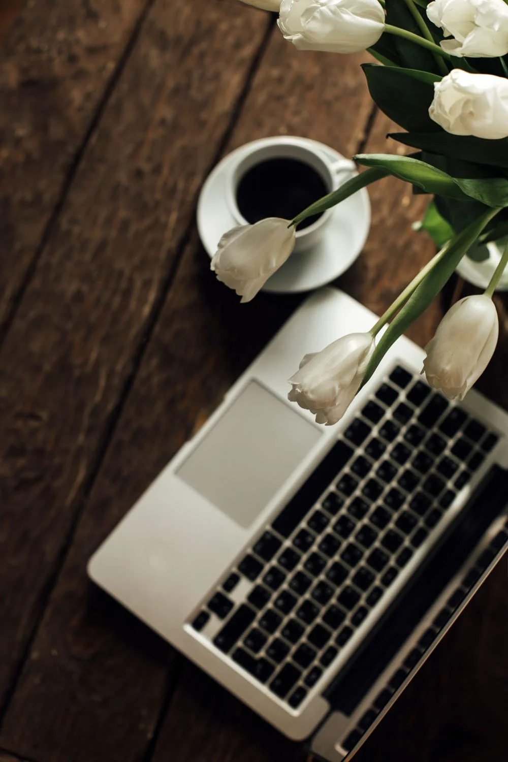 overhead view of computer, coffee, and white tulips