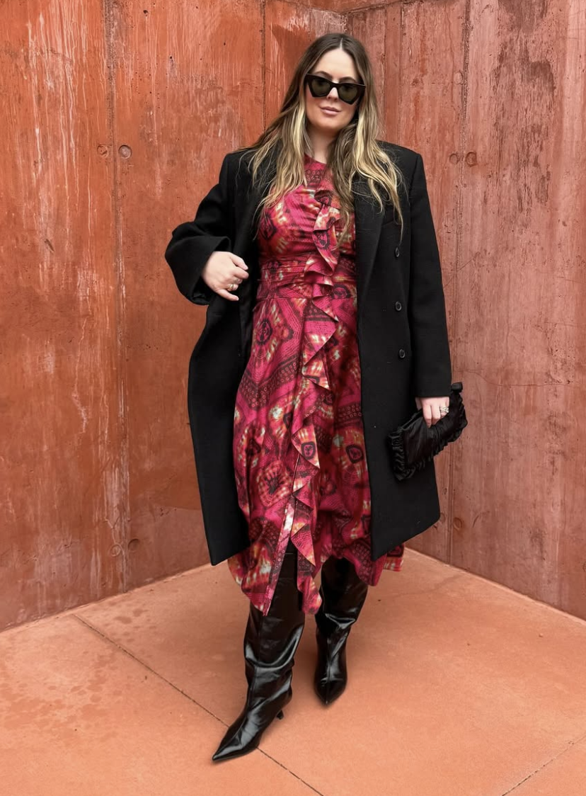 A smiling woman with long, wavy blonde hair, wearing a textured gray top, posing against a plain light background.