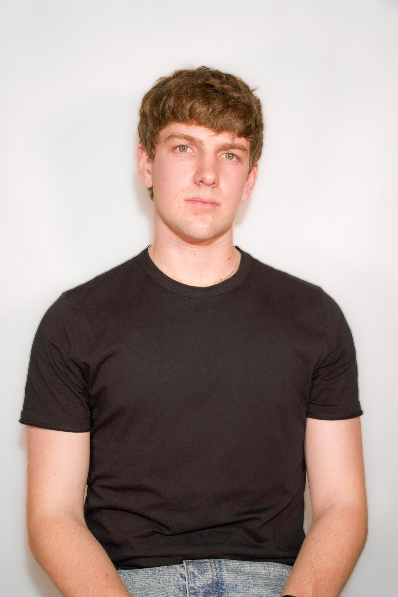 A young man with brown hair, green eyes, wearing a black T-shirt and jeans, standing against a plain white background.