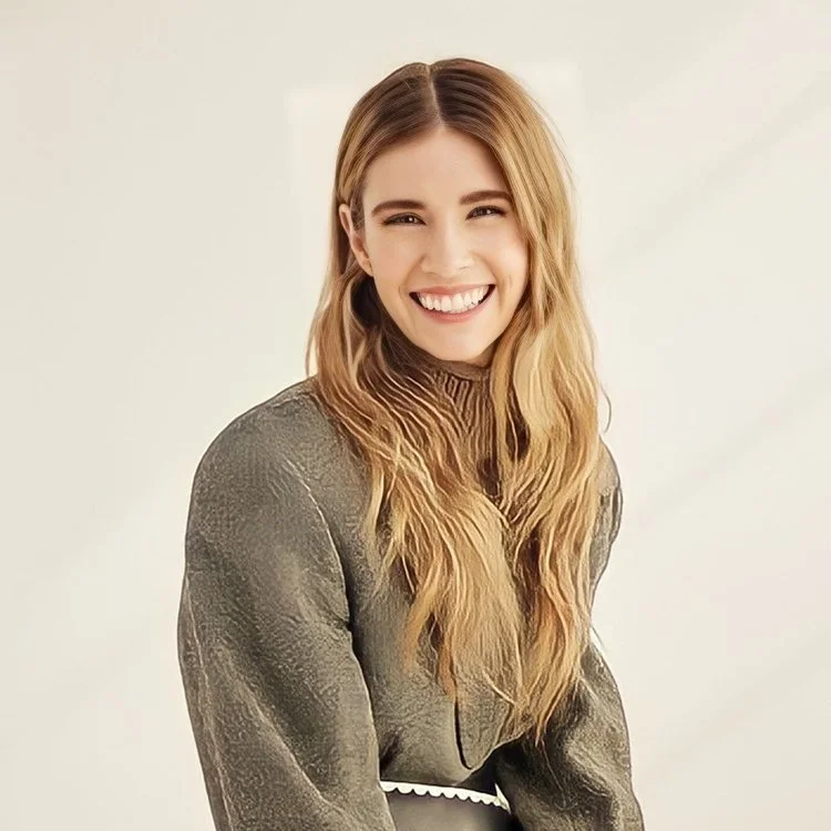 A smiling woman with long, wavy blonde hair, wearing a textured gray top, posing against a plain light background.