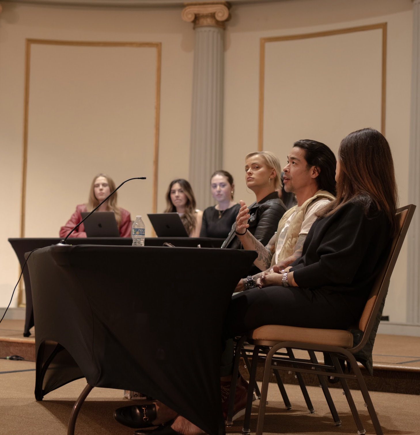 A panel of five people sitting at a table in a conference room, with one person speaking into a microphone.