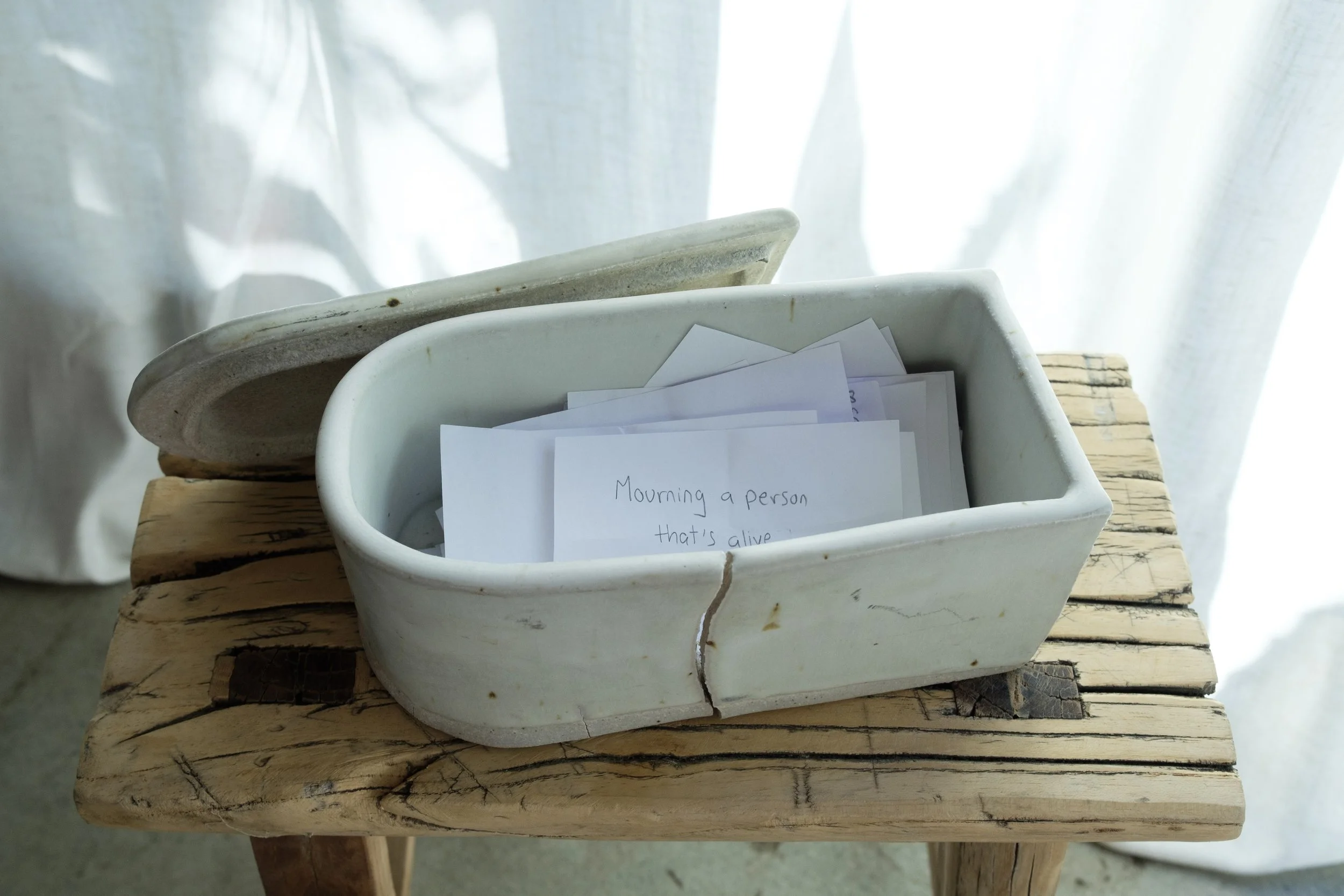 Open ceramic box with notes and poems inside on rustic wooden table, background of light curtains.
