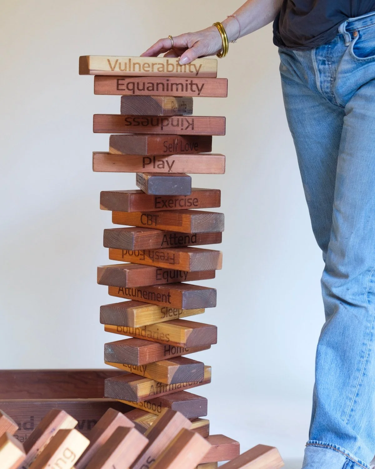 A hand placing a wooden block engraved Vulnerability on a tall stacked tower