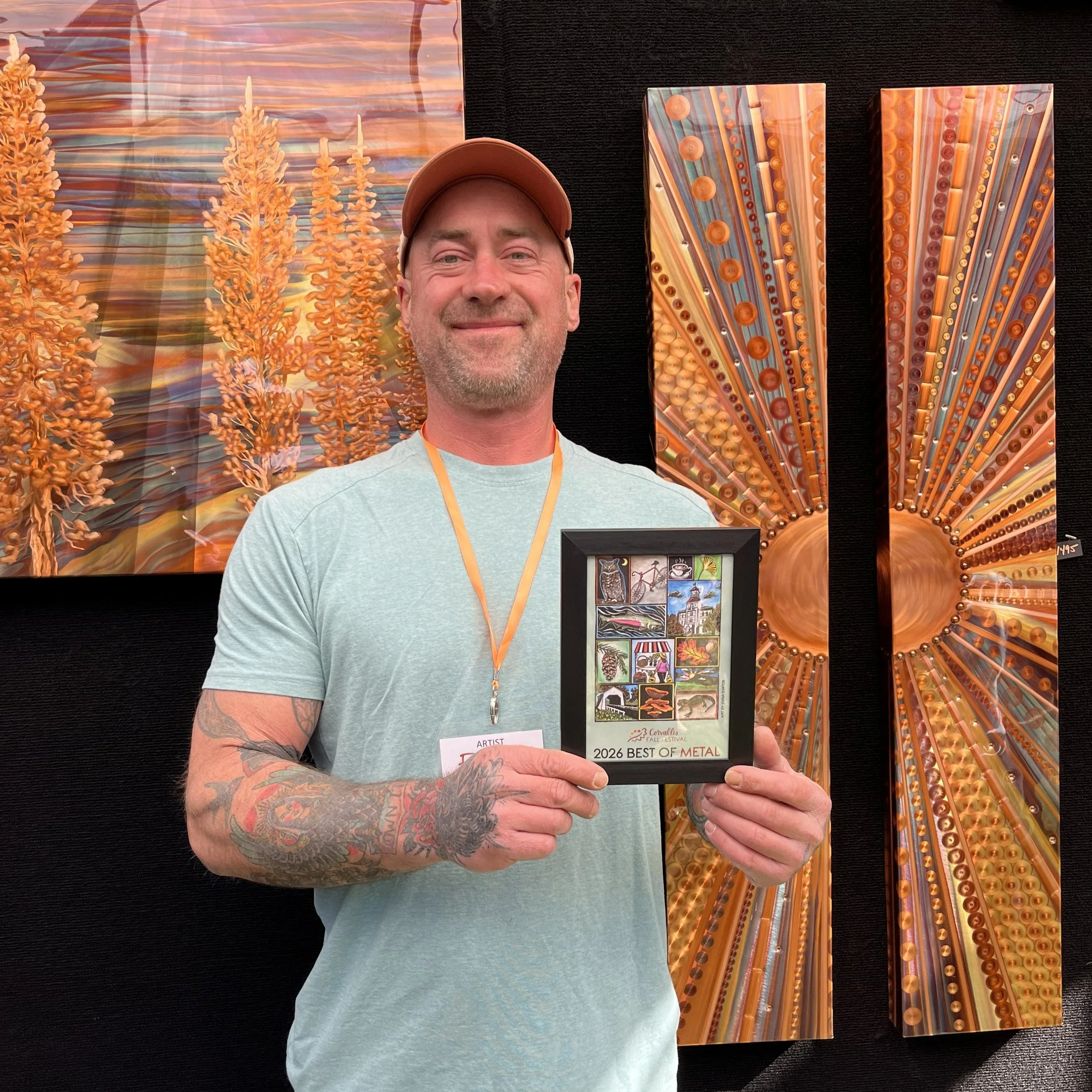 A man smiling and holding a framed Corvallis Fall Festival poster that reads "2026 best of metal."