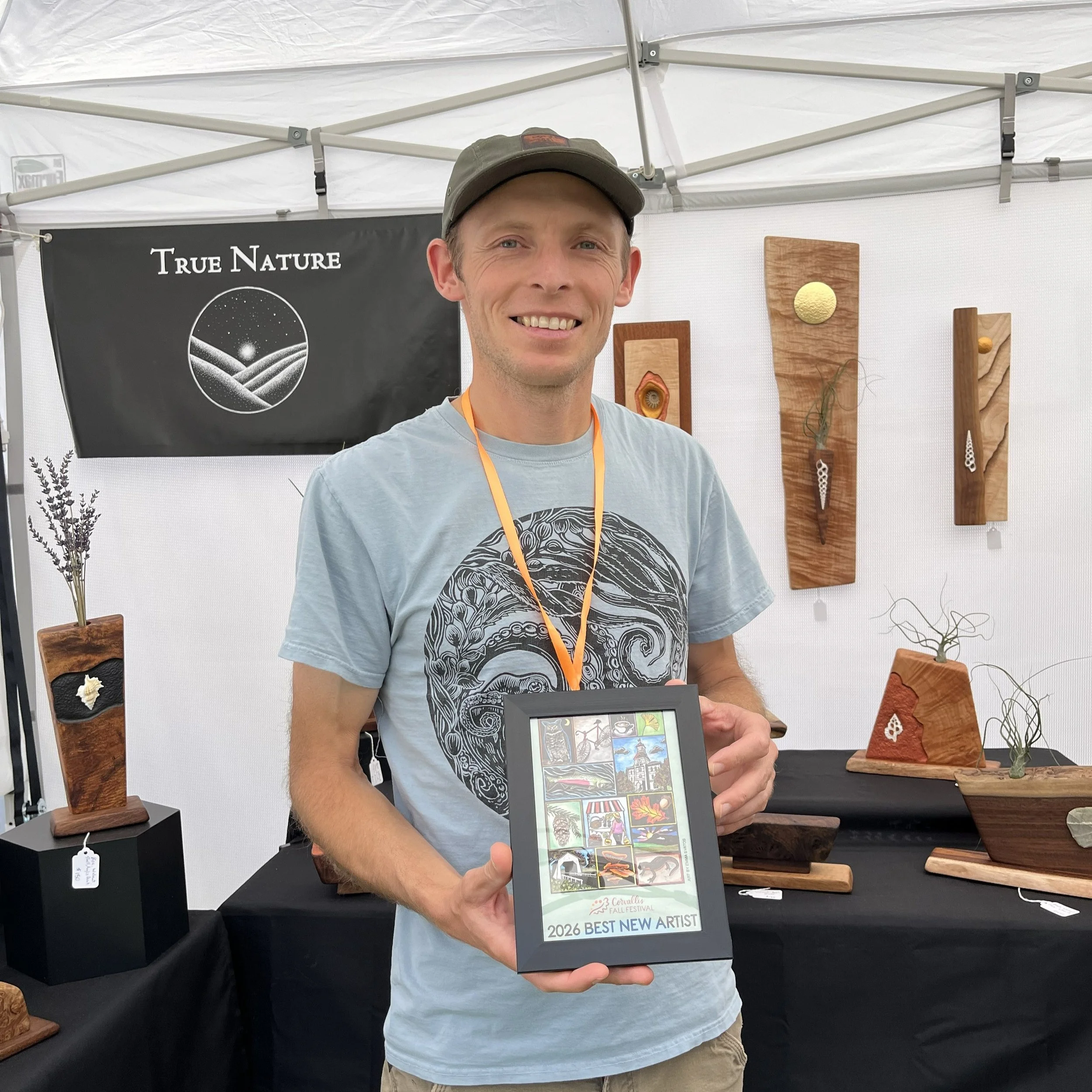 A man smiling and holding a framed Corvallis Fall Festival poster reading "2026 Best new artist."