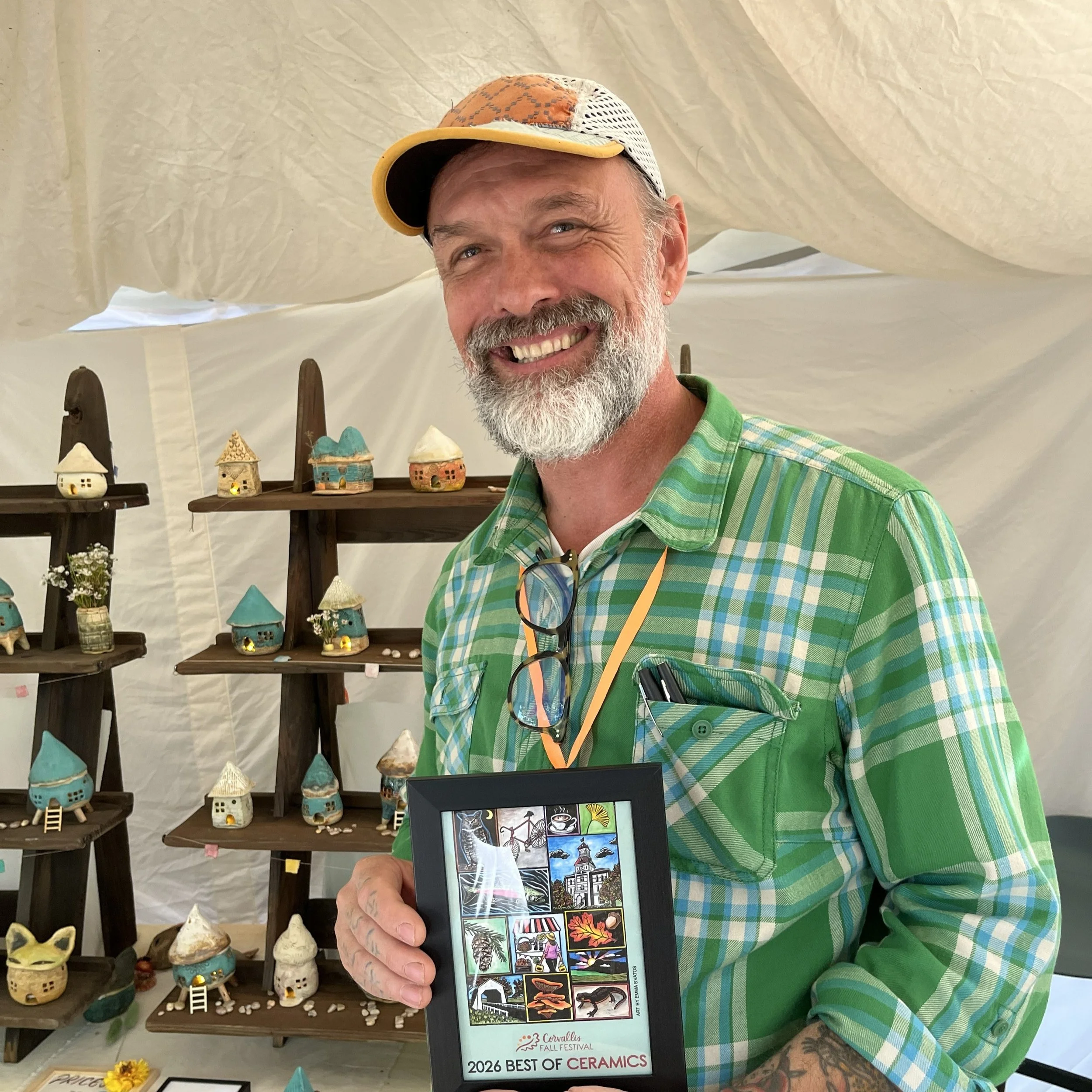 A man smiling and holding a framed Corvallis Fall Festival poster that reads "2026 best of ceramics."