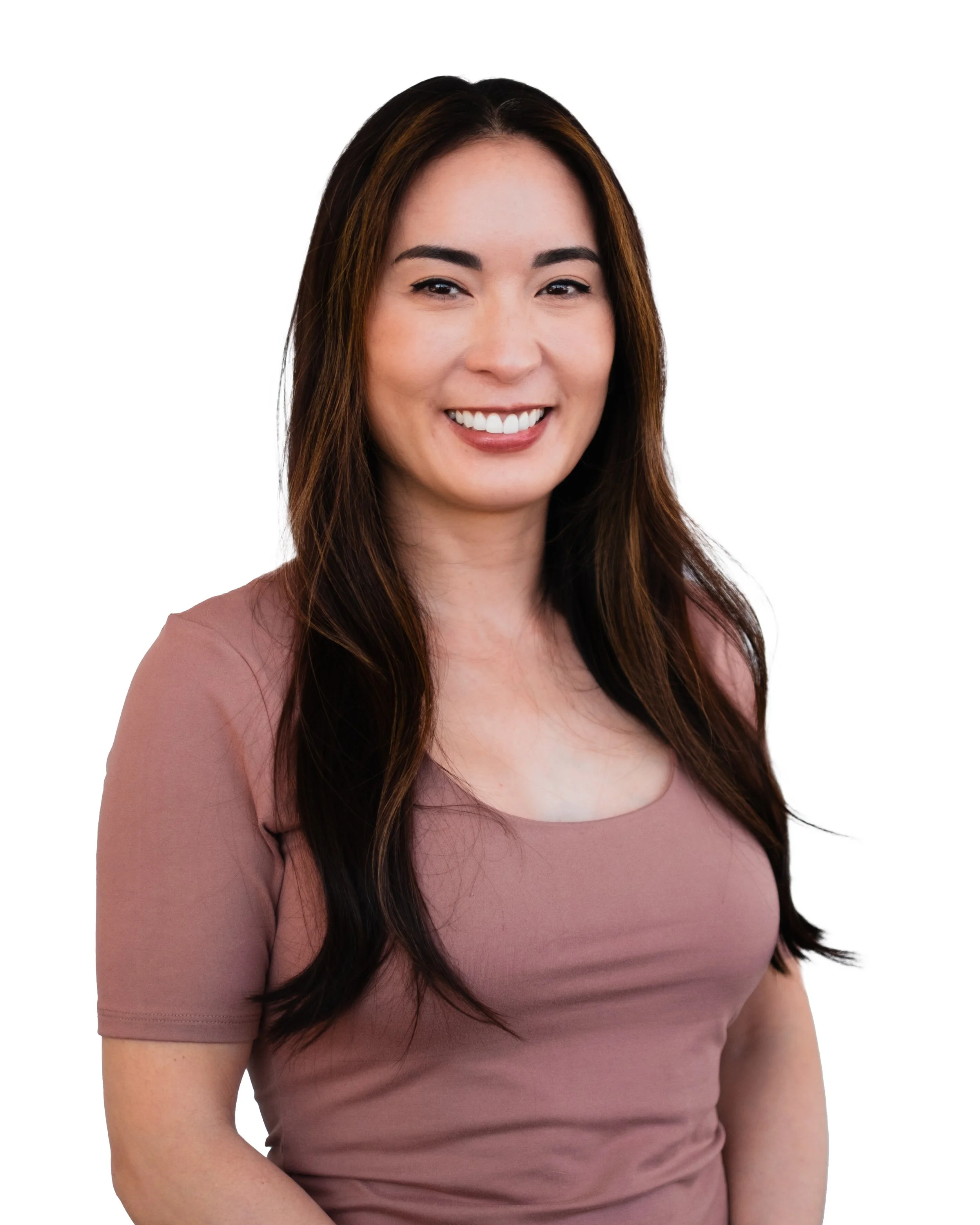 A smiling woman with long dark hair wearing a short-sleeved light mauve top, standing against a plain white background.