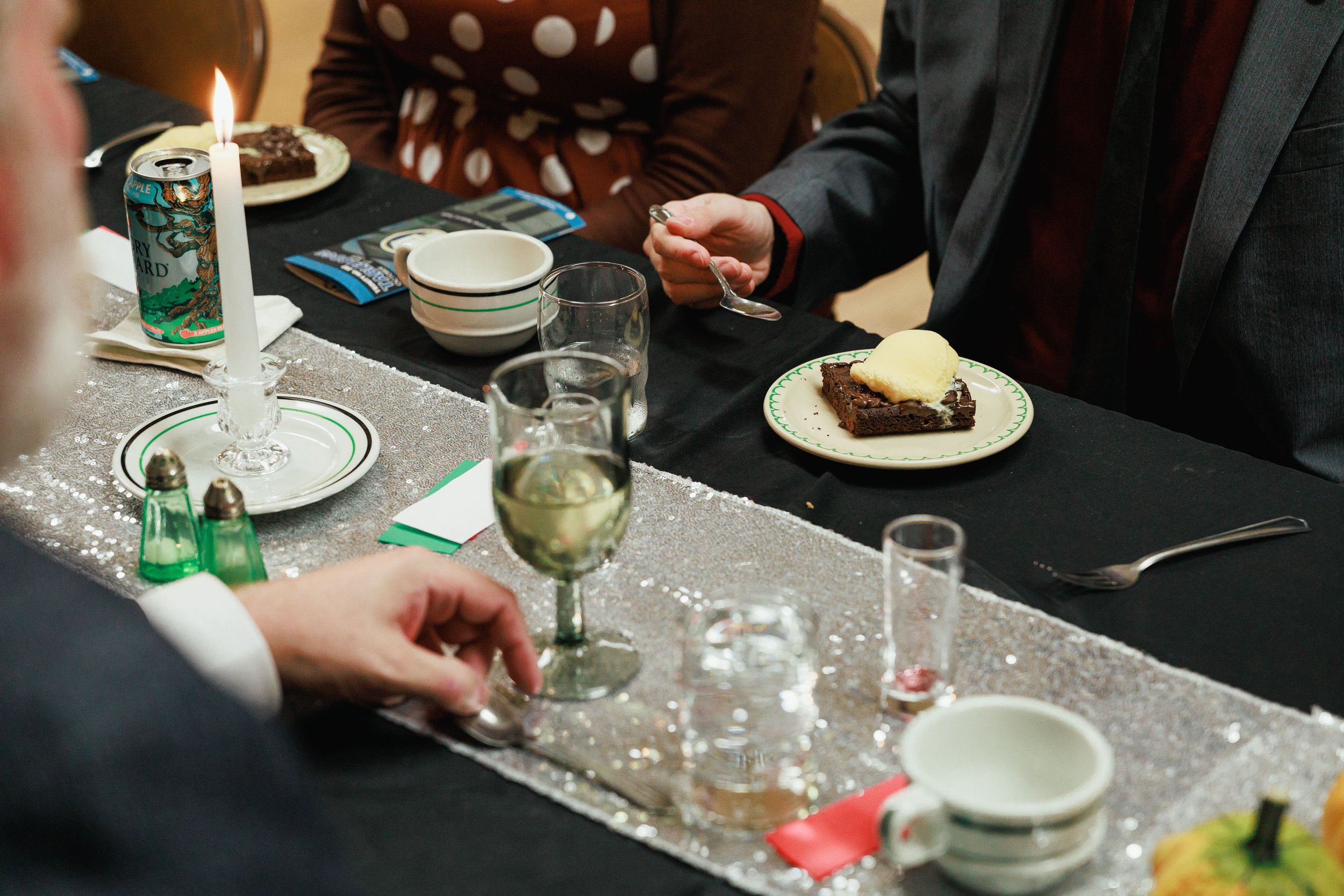 People sitting at a table with desserts, drinks, and a lit candle, celebrating a special occasion.