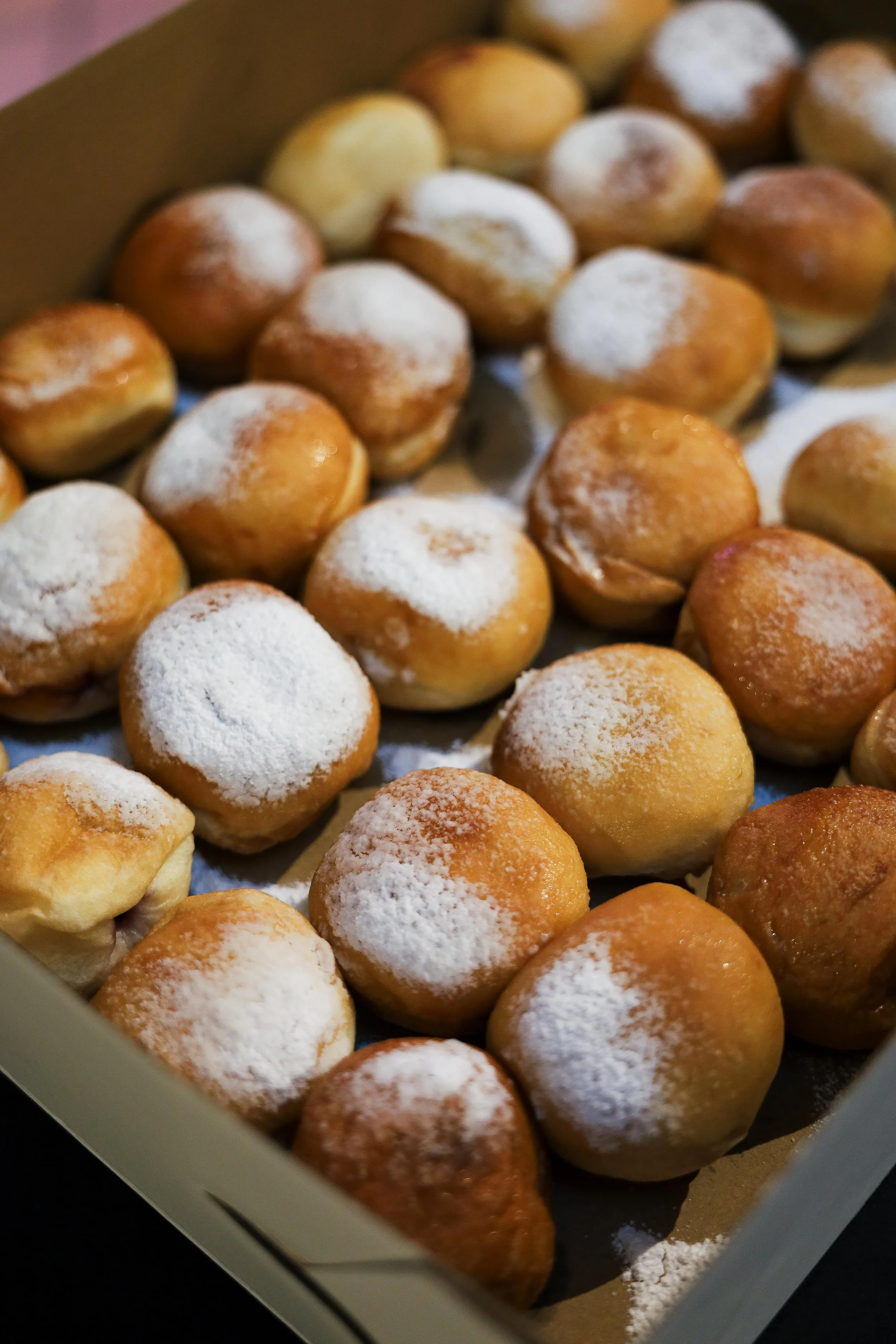 A box of freshly baked cream puffs topped with powdered sugar.
