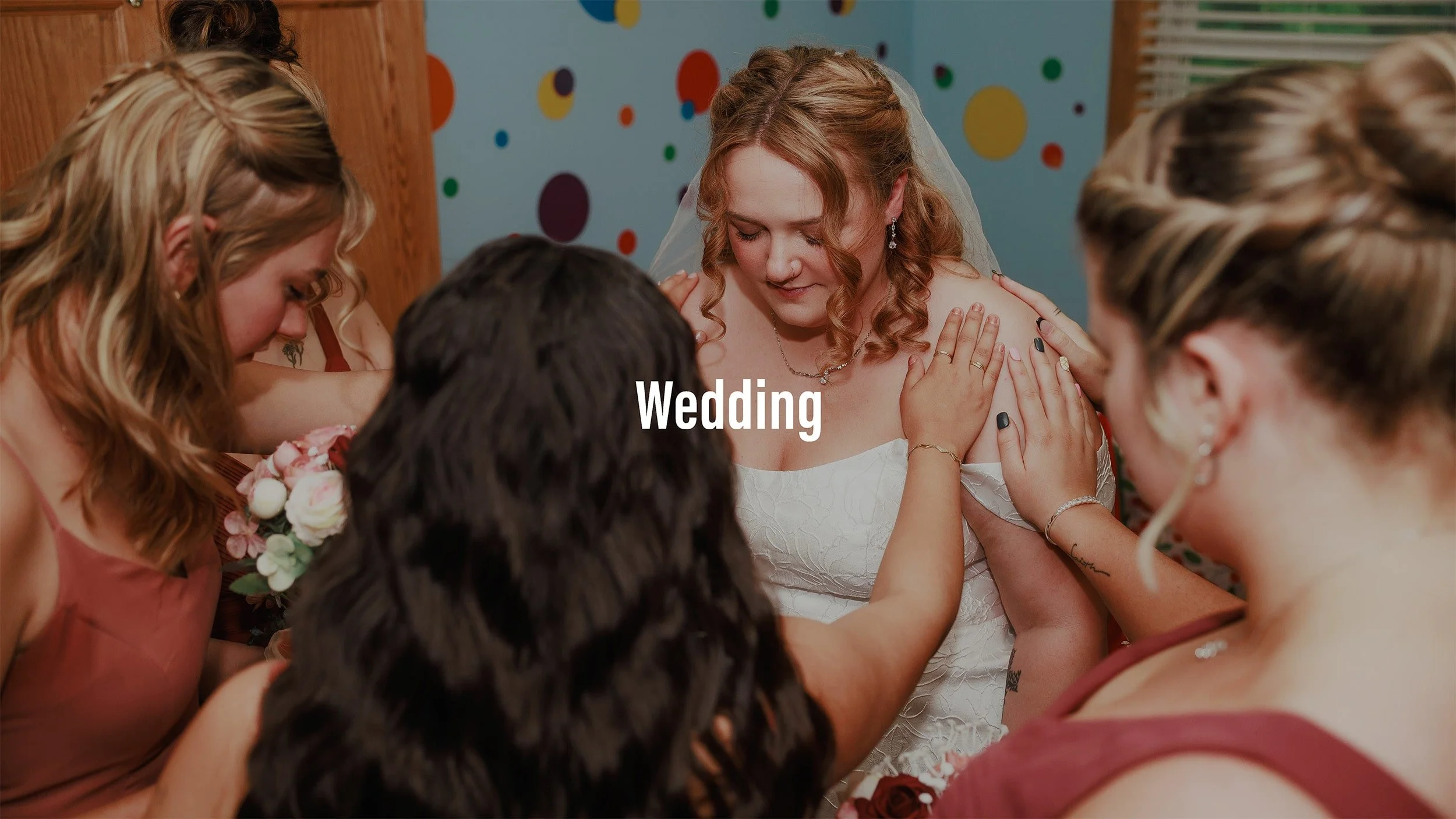 A bride in a white wedding dress surrounded by bridesmaids in reddish-brown dresses during a heartfelt moment at a wedding.