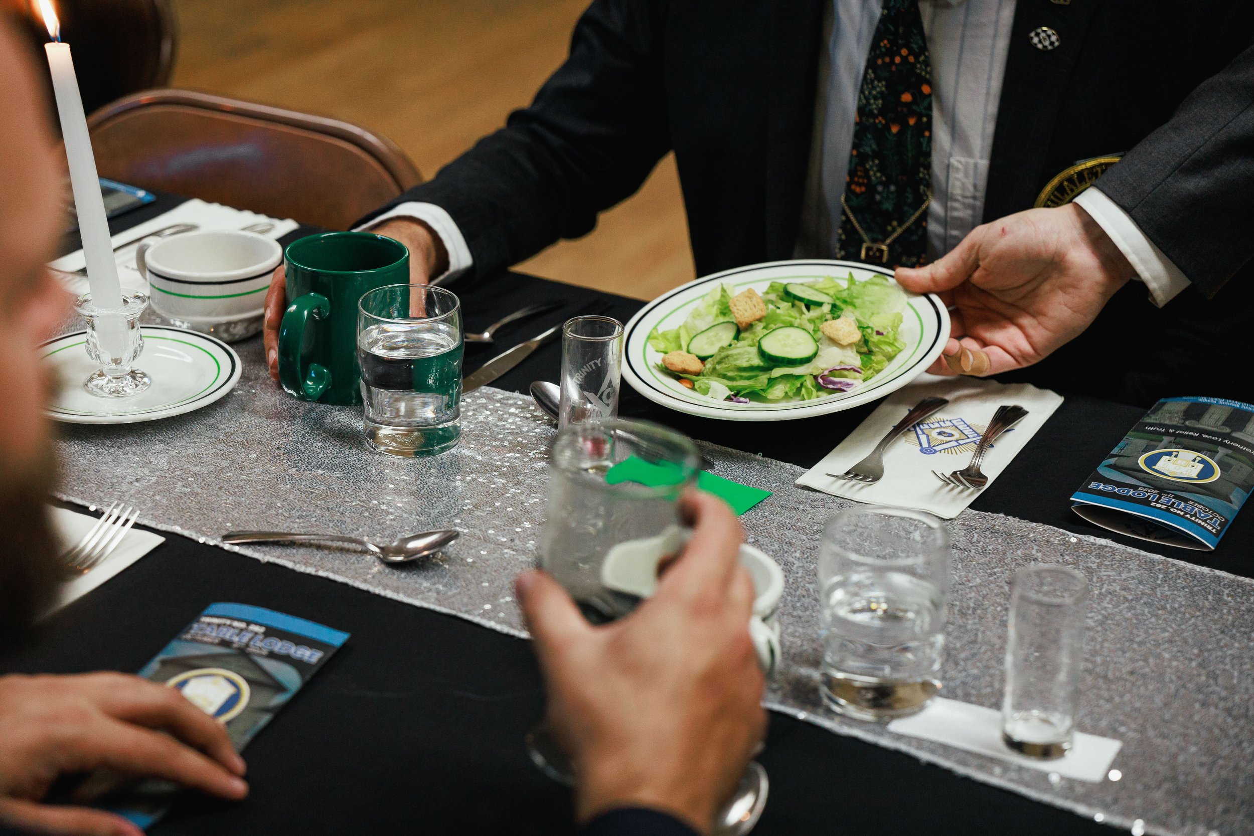 Person serving a salad with cucumber, lettuce, and croutons at a formal dinner event.