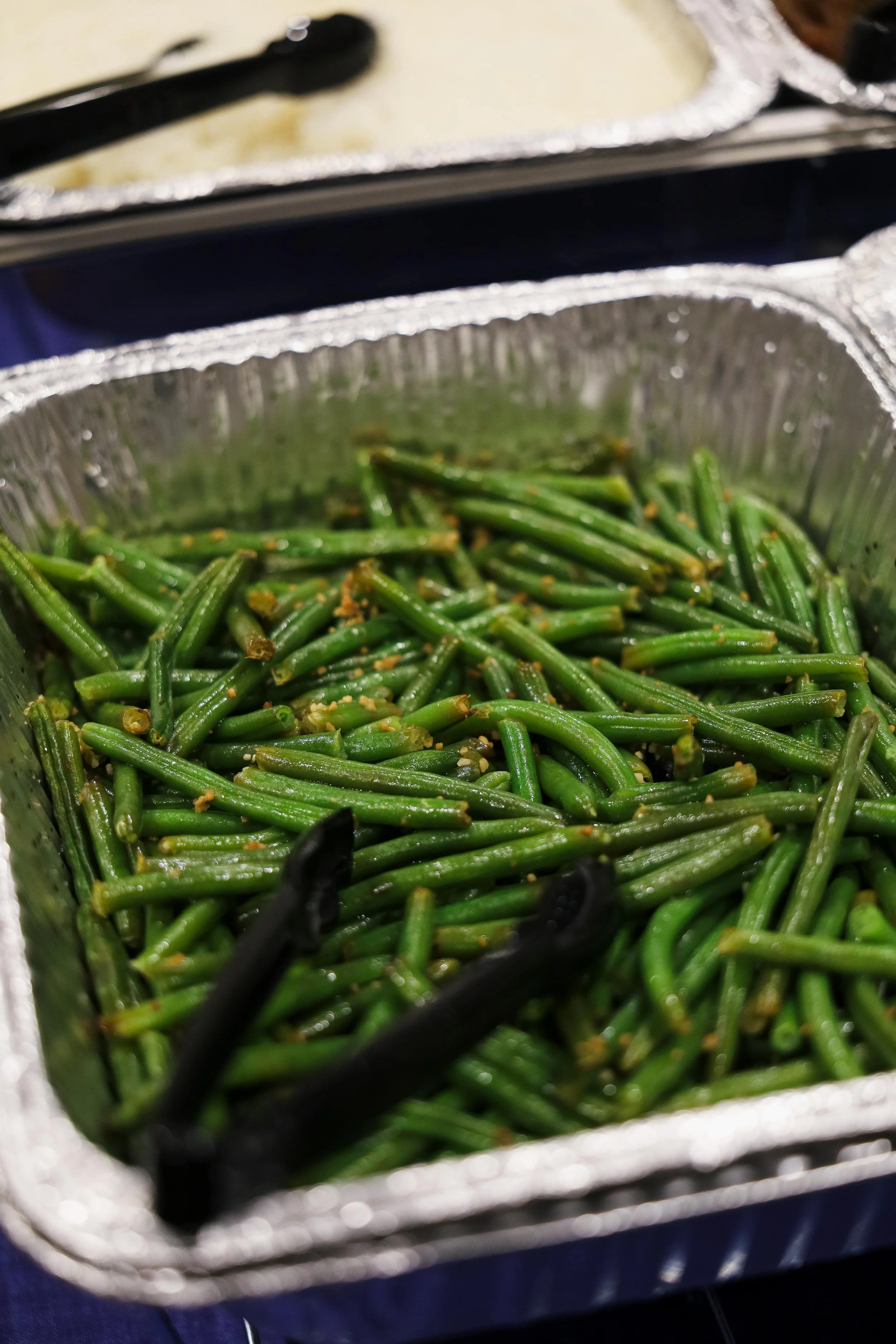 Aluminum tray full of cooked green beans with garlic.
