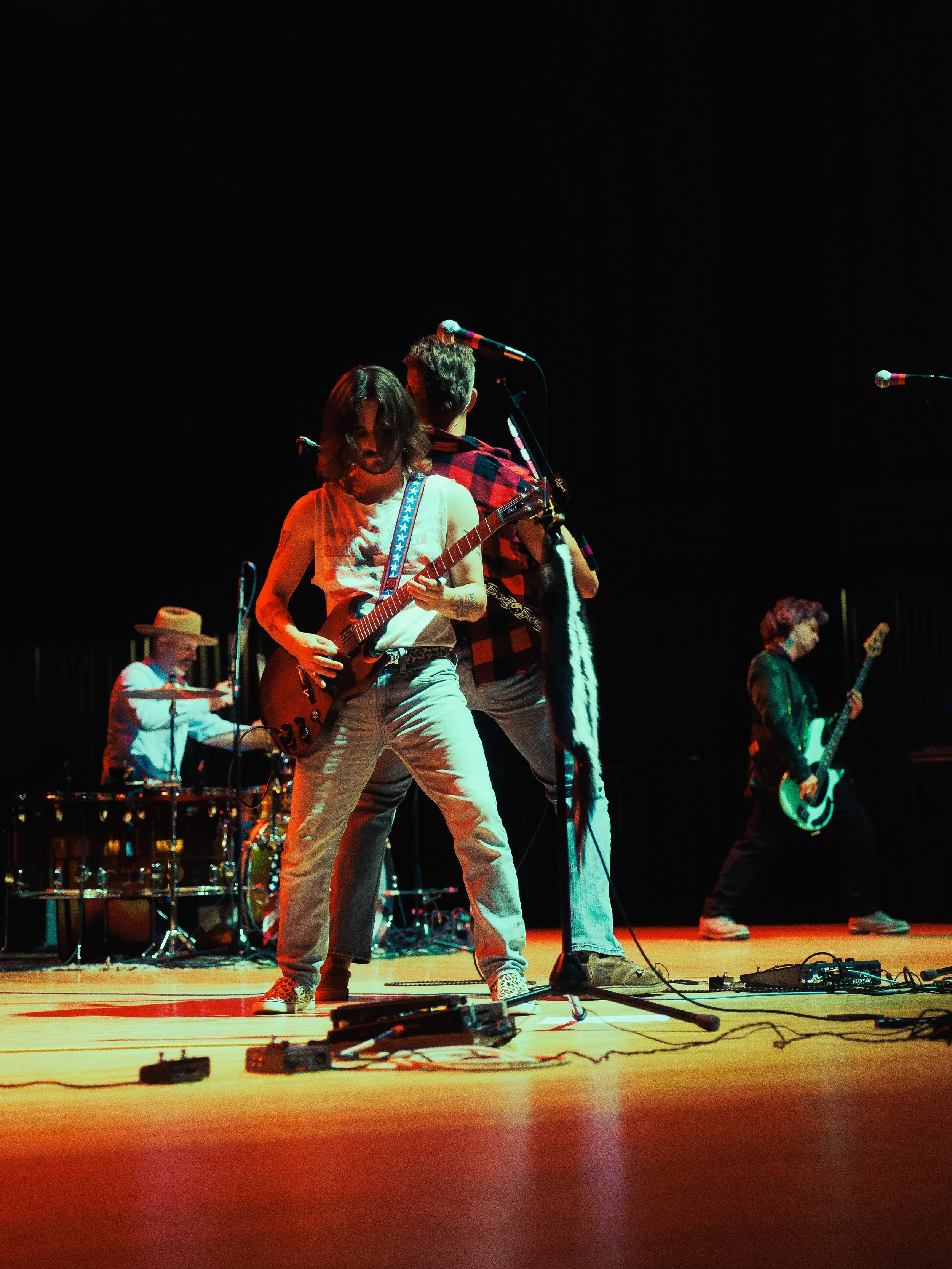 Musicians performing on stage with guitars and drums, stage lights illuminating them against a dark background.