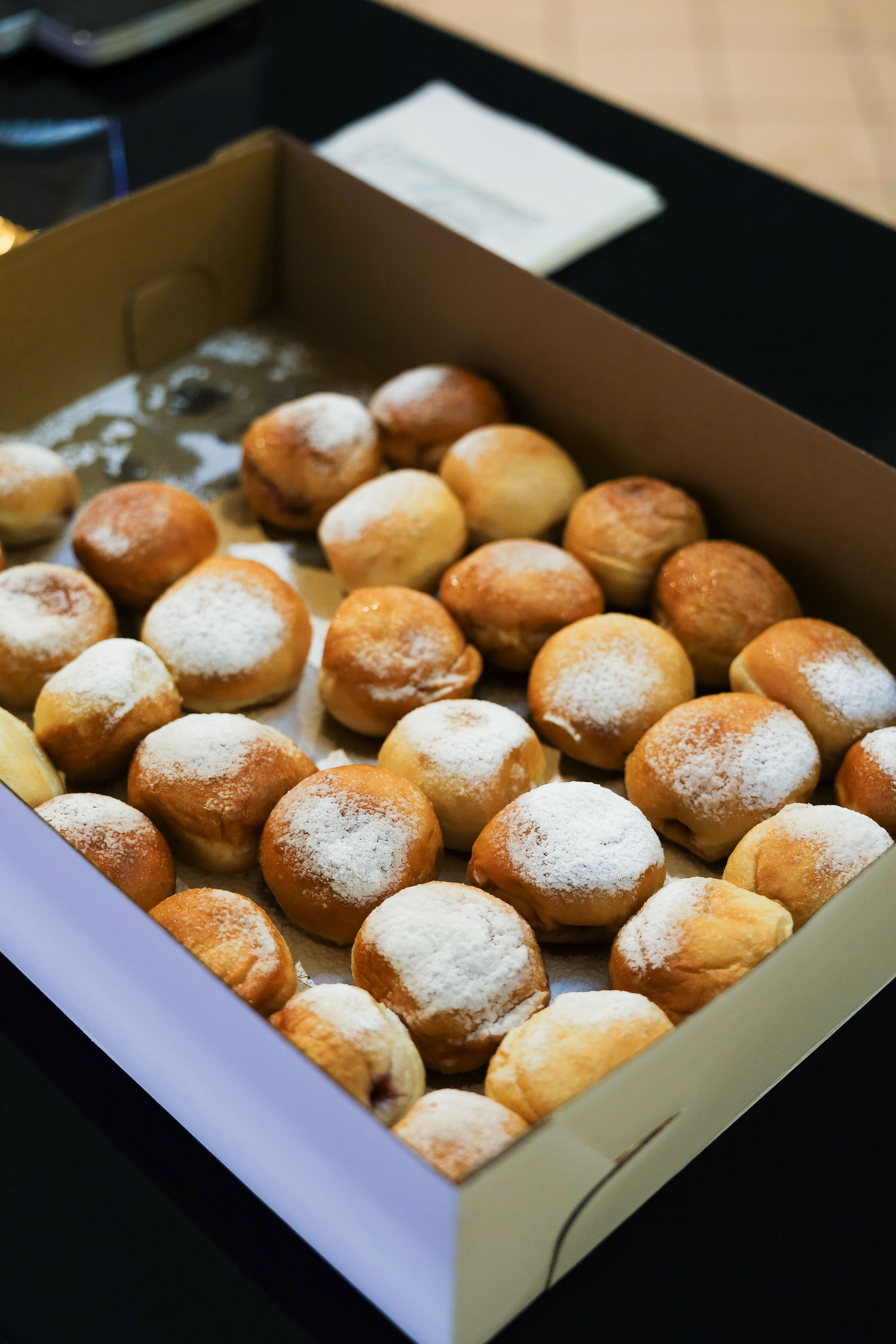 A box of powdered sugar-covered donut holes on a black table.