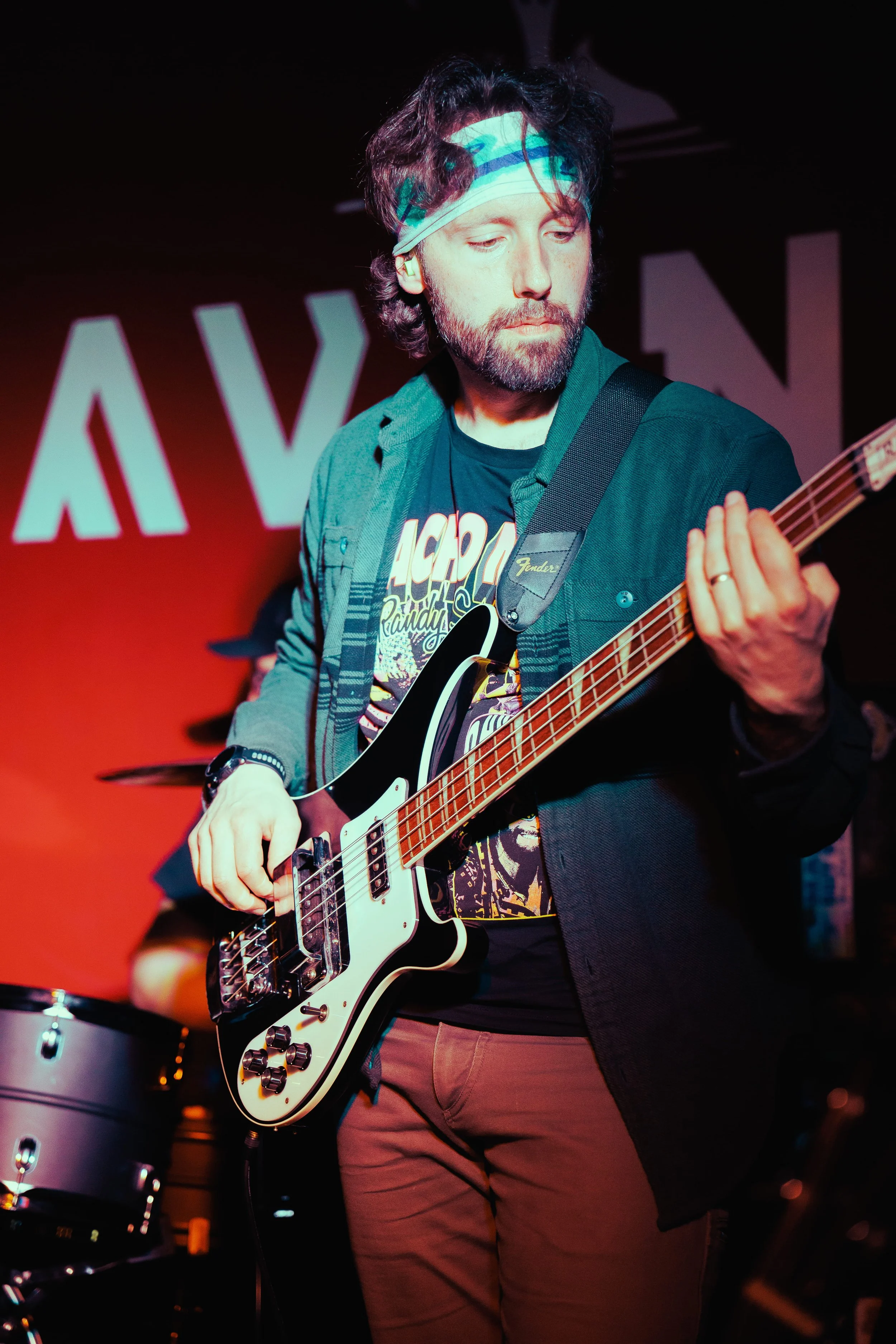 A man with a beard and curly hair wearing a headband, playing an electric guitar on stage during a performance.