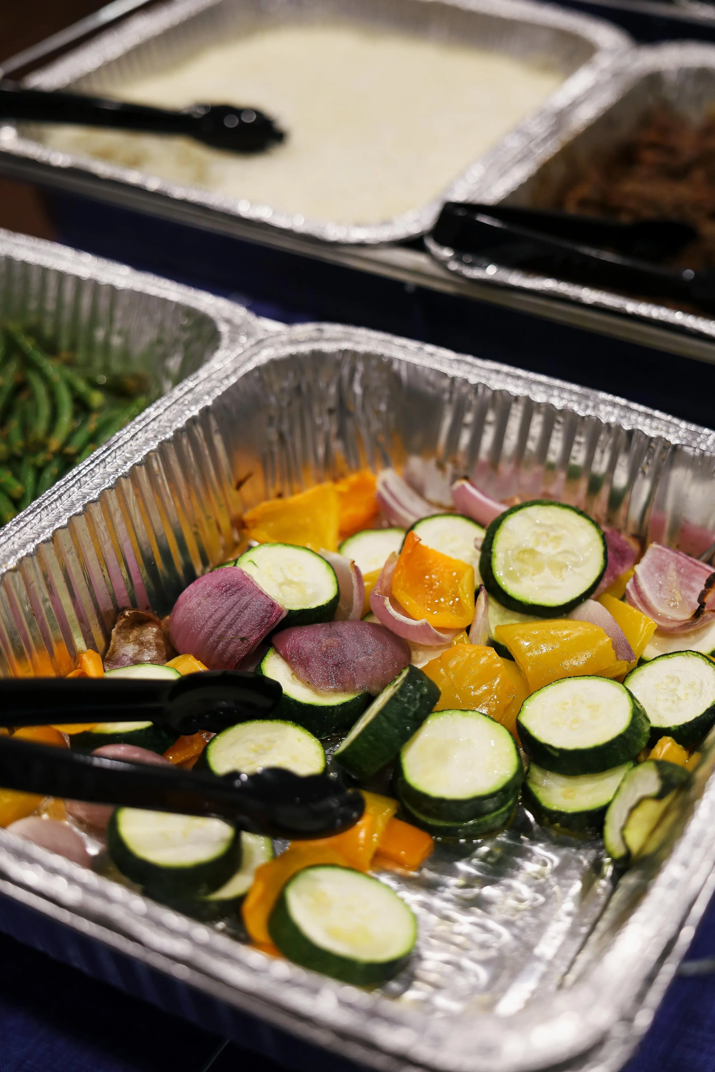 Aluminum tray with chopped zucchini, yellow bell peppers, and red onions.