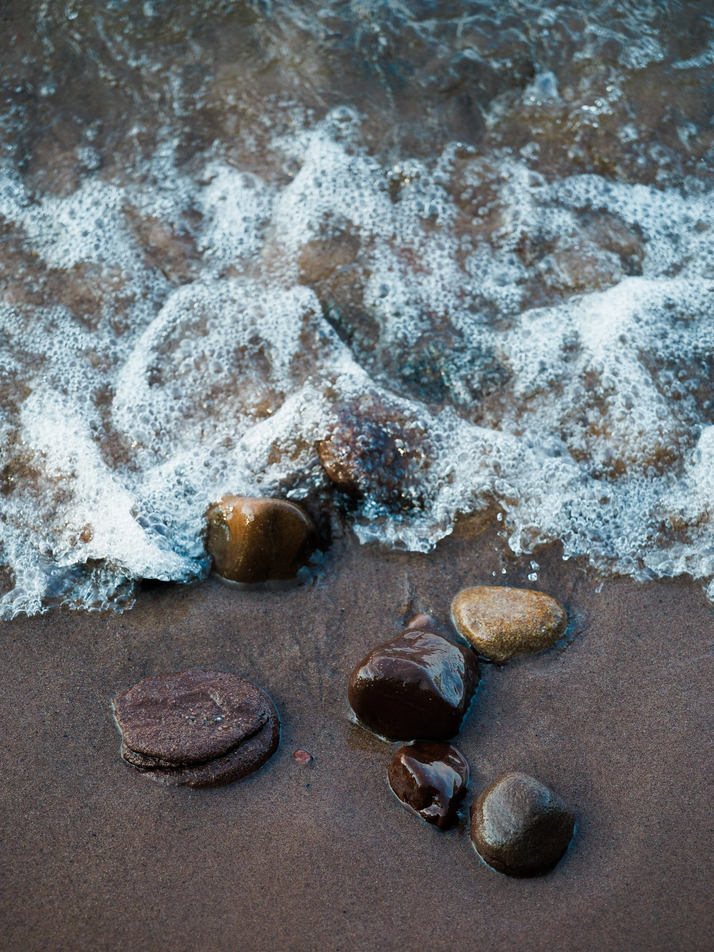 Rocks on a sandy beach with small waves washing over them.