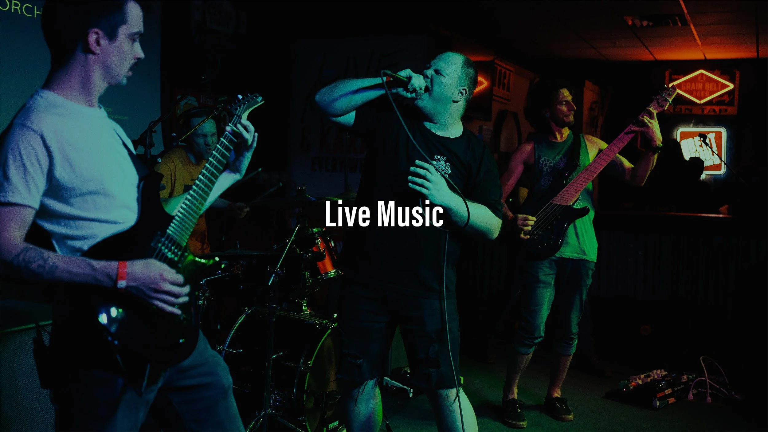 Band performing live music on stage with guitar, bass, and microphone in a dimly lit venue with neon signs