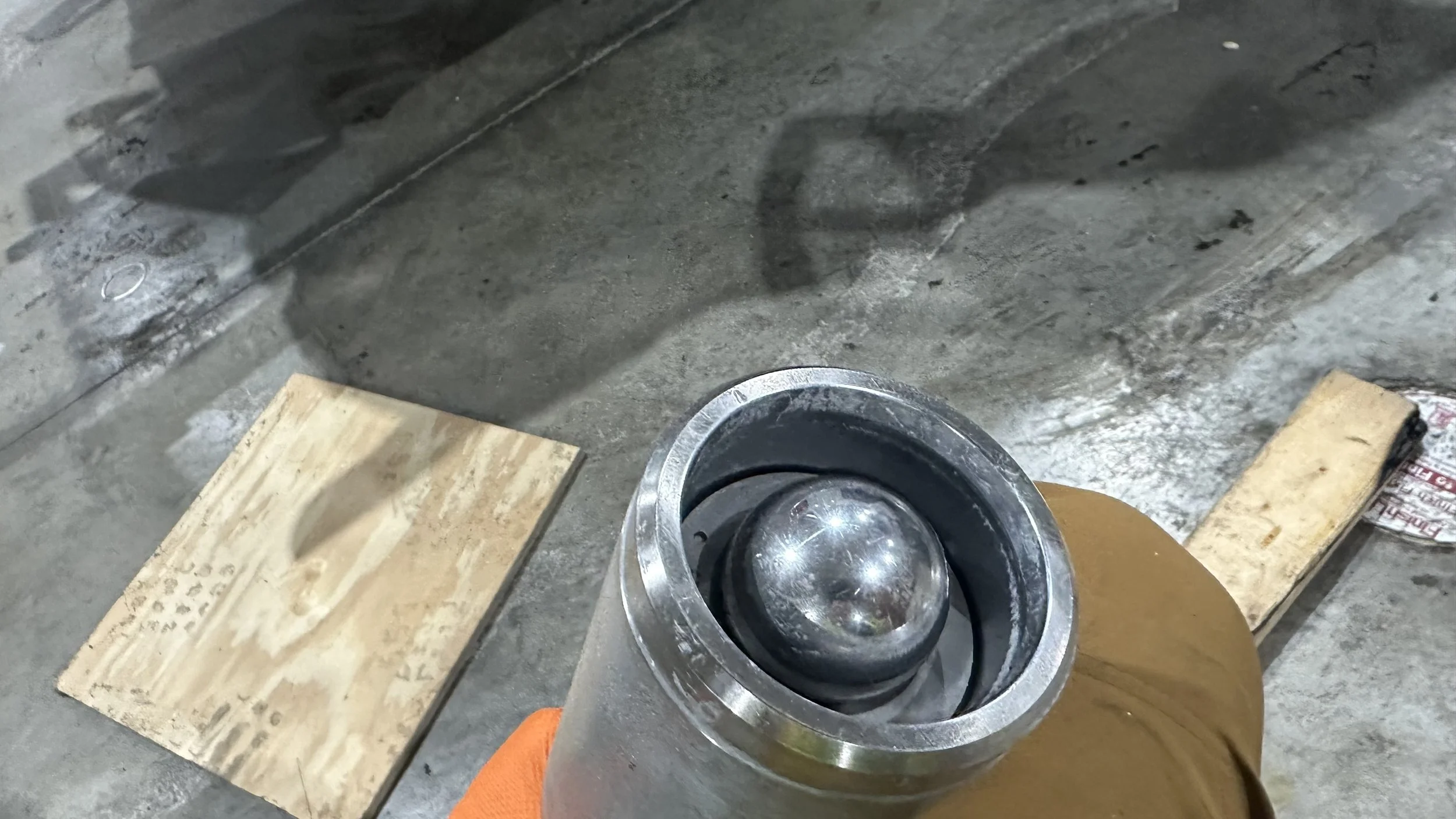 Close-up of a person holding a metal bearing or industrial part over a concrete floor with wooden blocks and other tools in the background.