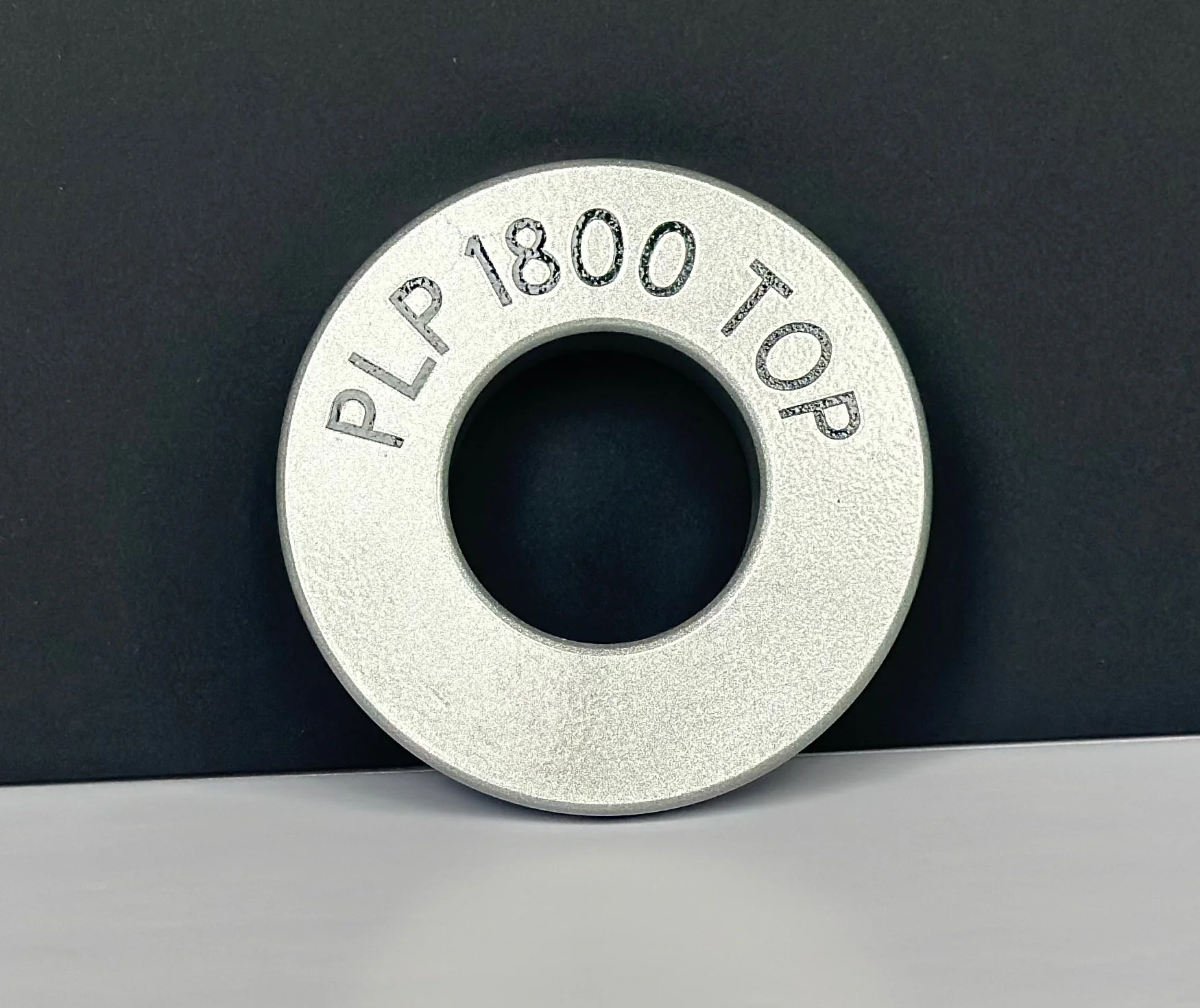 A metallic centering ring with engraved text reading 'PLP 1800 TOP' on its surface, positioned against a dark background.