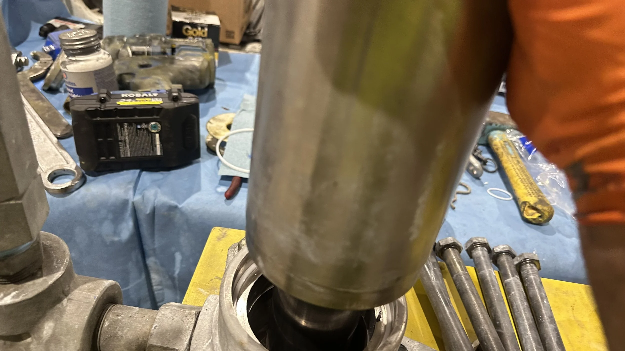 Close-up view of a mechanical or automotive component with tools and parts scattered on a blue work surface in the background.