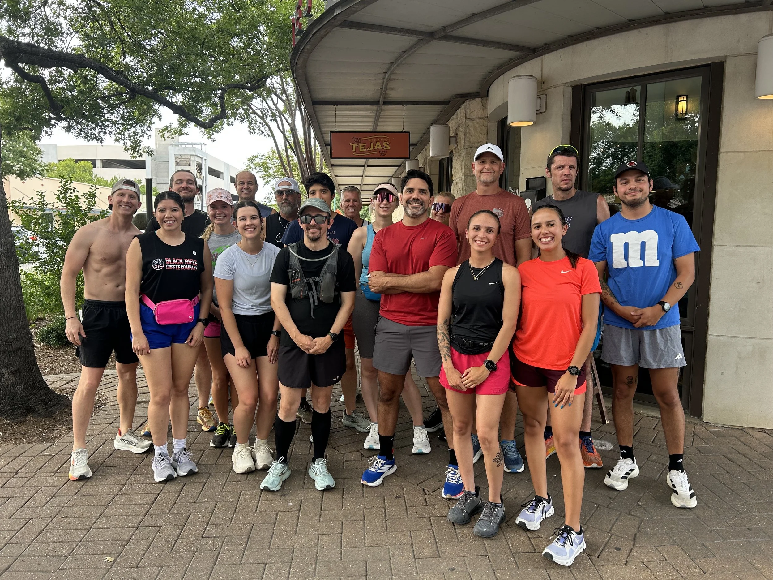 Group of runners posing outdoors in front of a building with trees in the background.