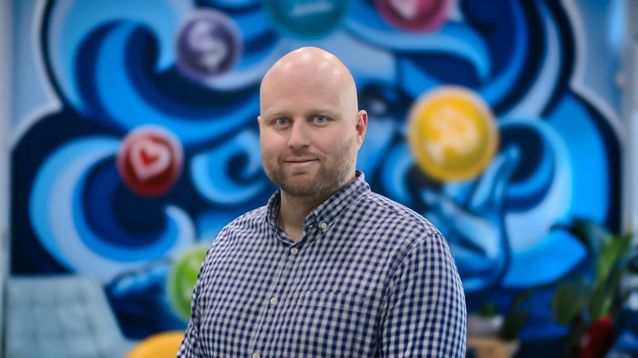 Director Phil McCredden, smiling at camera in front of colourful blue and yellow mural. Located in Bunbury office.