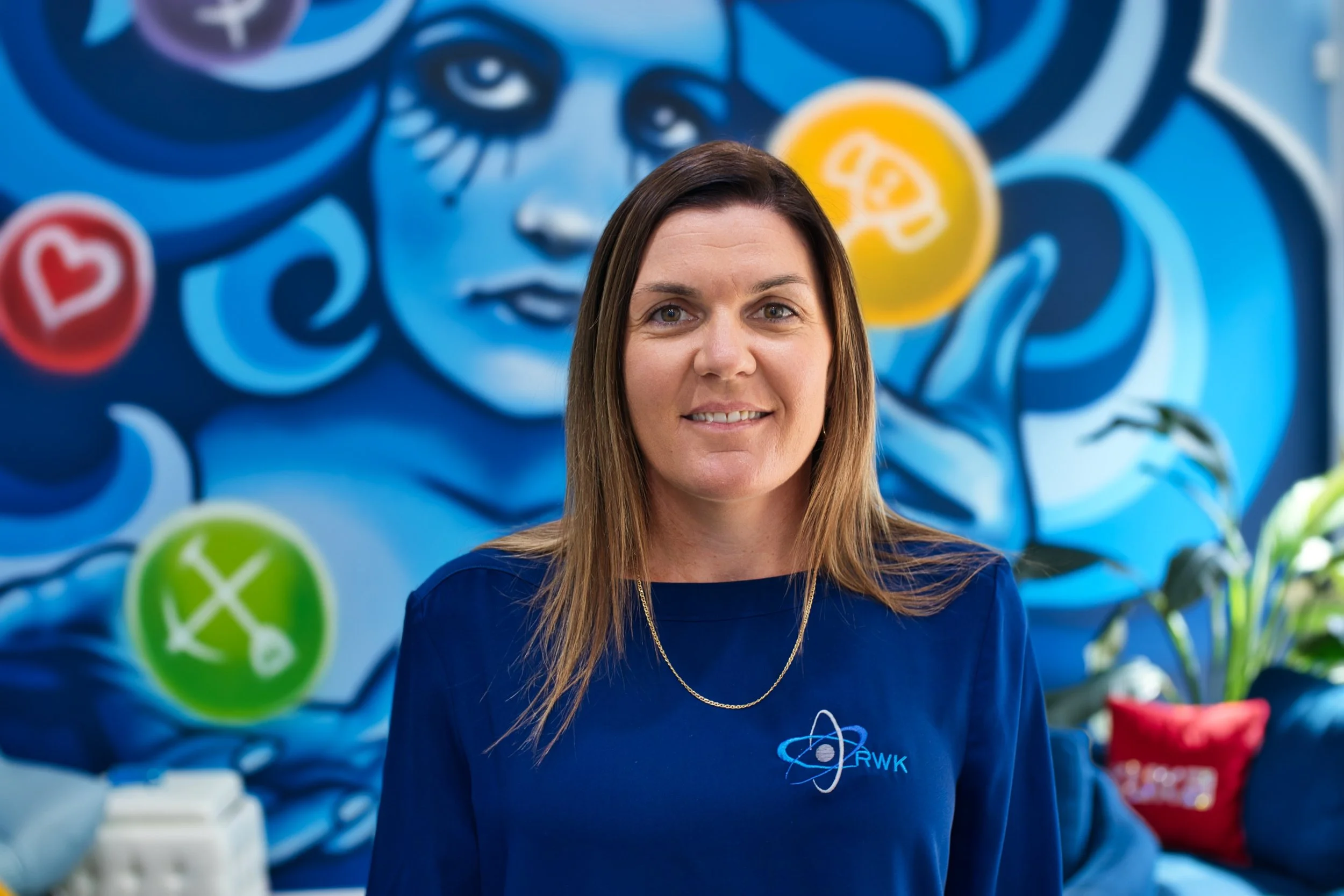 Client Services, Rebecca, smiling at camera in front of colourful blue and yellow mural. Located in Bunbury office.
