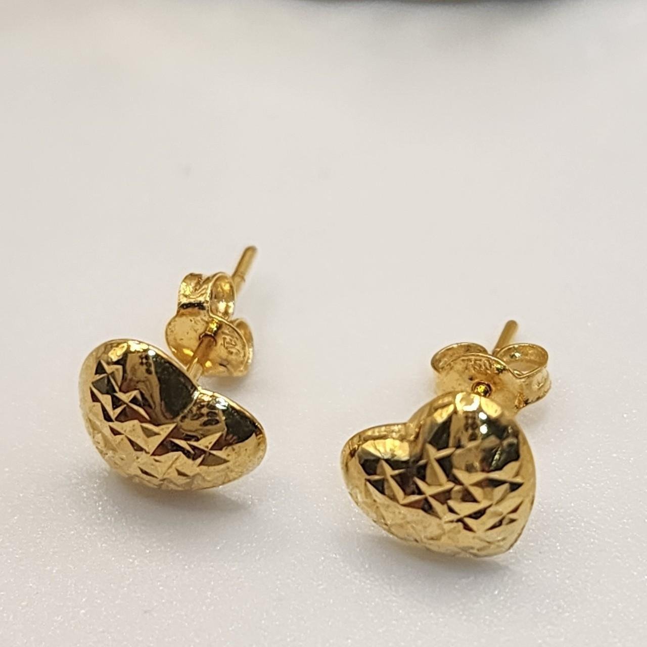 Gold heart-shaped earrings with a textured pattern, placed on a white surface.