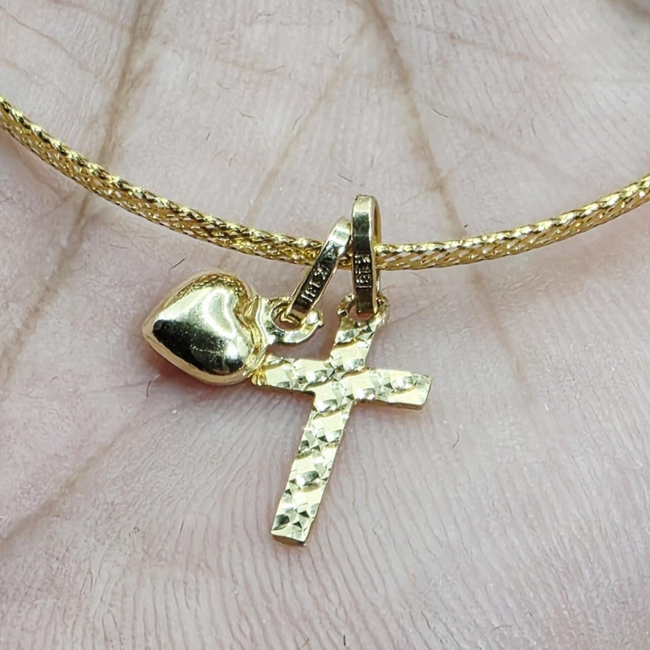 Close-up of a gold necklace with a cross pendant and a small heart charm, worn on a person's neck.