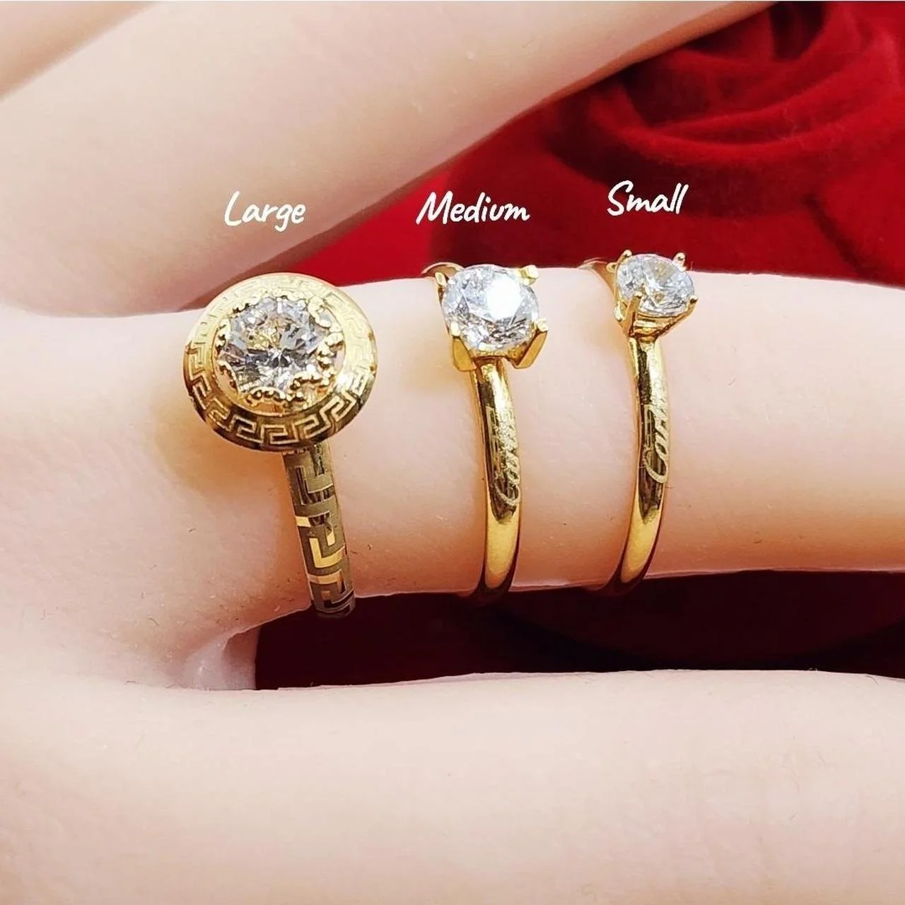 Three gold rings with large, medium, and small diamonds, labeled accordingly, worn on a finger against a red background.