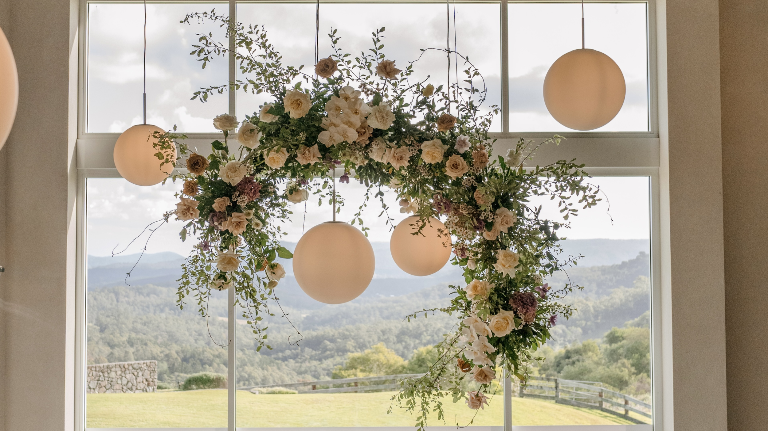 A floral arrangement with hanging spherical lights suspended in front of large windows with scenic mountain views.