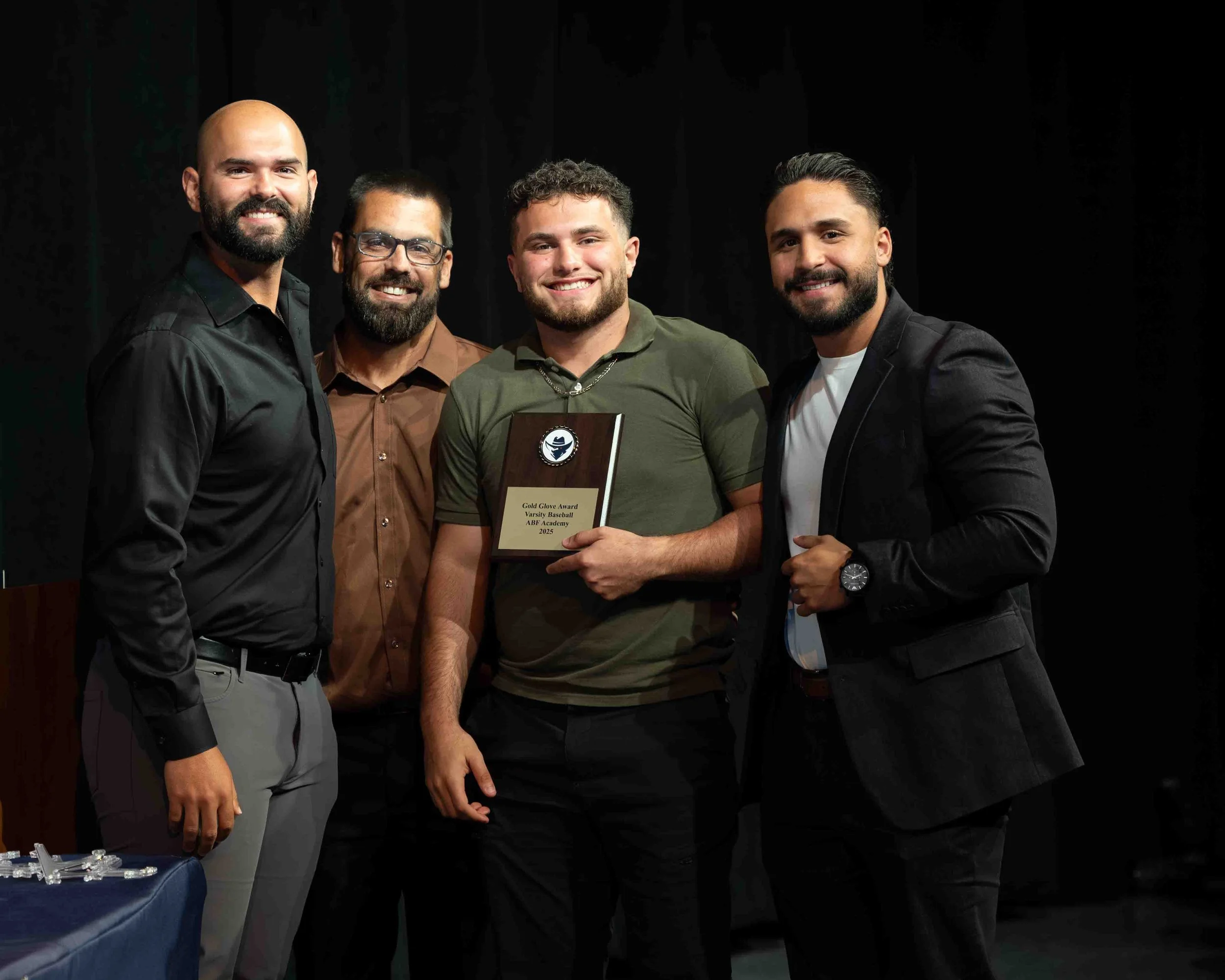 Four men standing together, one holding a plaque, at an awards ceremony, smiling in front of a dark background.