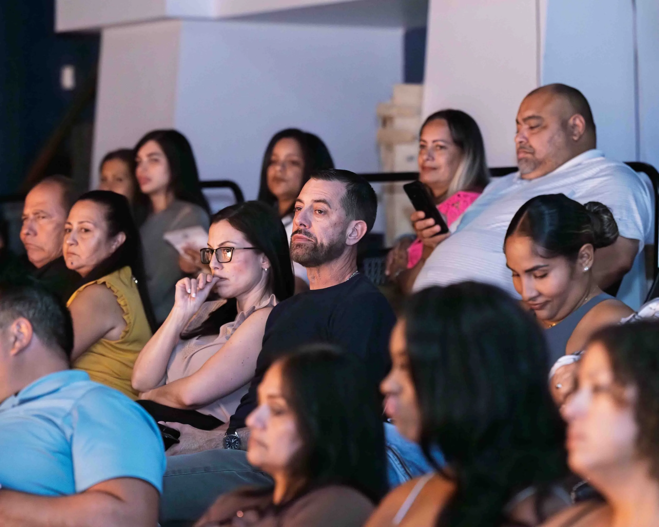 A group of diverse people sitting and listening attentively at an indoor event or seminar.