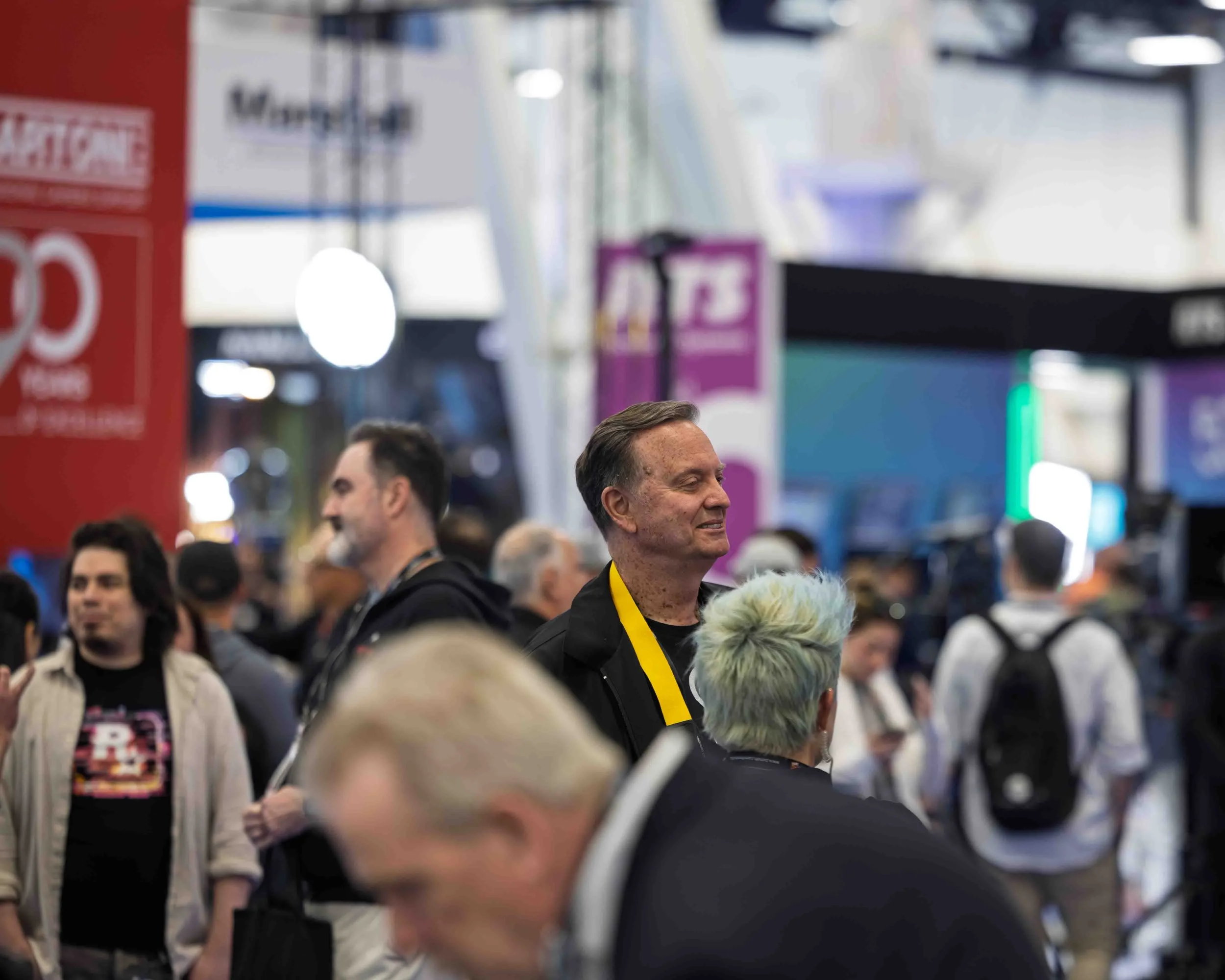 People attending a crowded corporate event or convention, with some conversations happening and booths in the background.