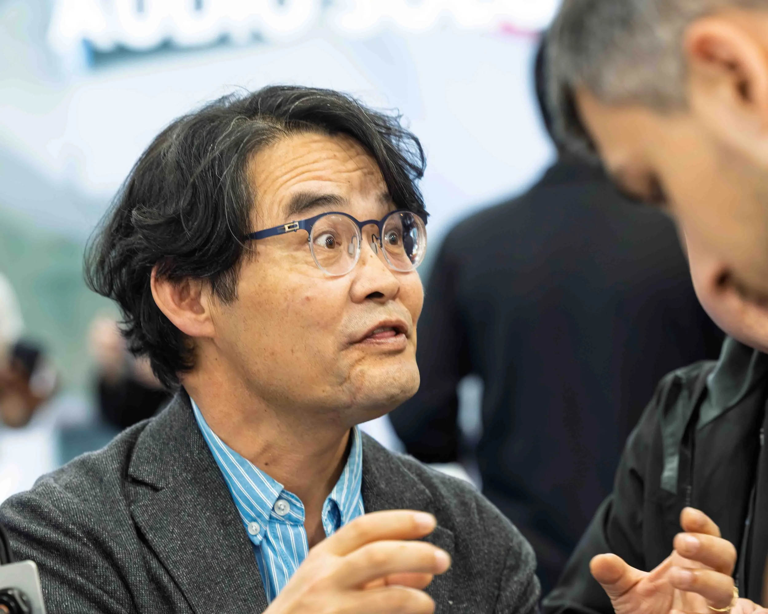 A man with glasses and wavy hair engaging in conversation with a woman in a black jacket in a crowded corporate event.