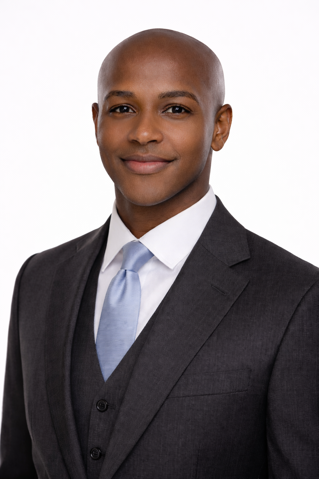 Headshot of a professional man with a shaved head wearing a dark suit, white shirt, and light blue tie, posing against a plain white background.