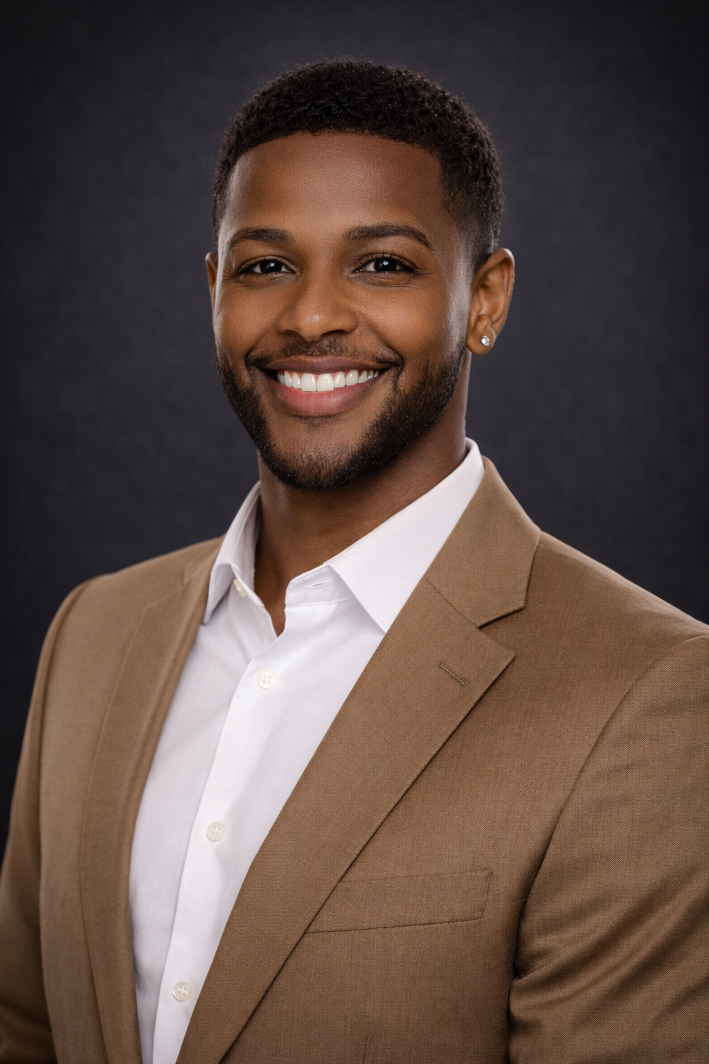 Headshot of a smiling man in a tan suit and white shirt against a dark background.