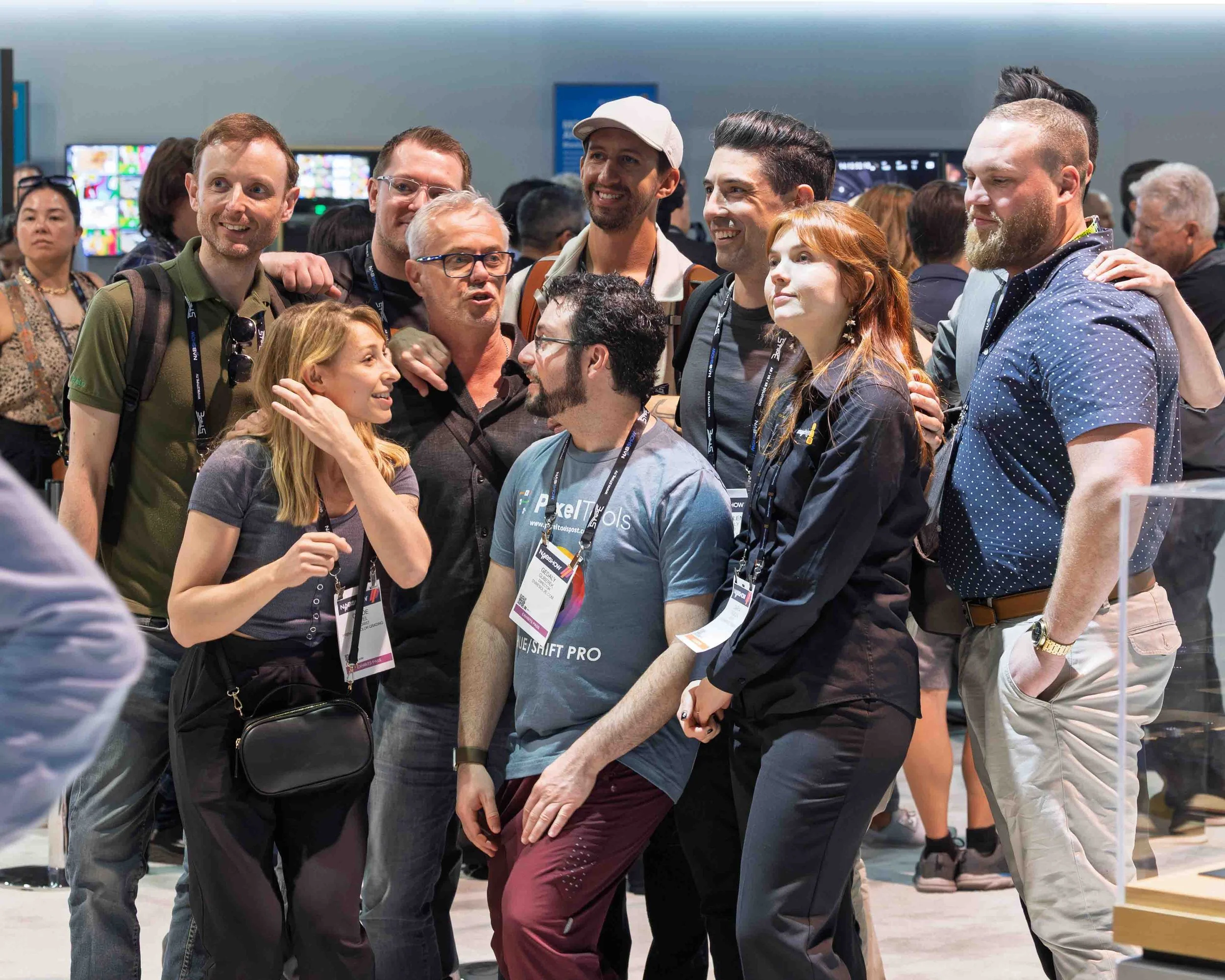 Group of diverse people at a conference or event, engaging in conversation and smiling, with many wearing conference badges.