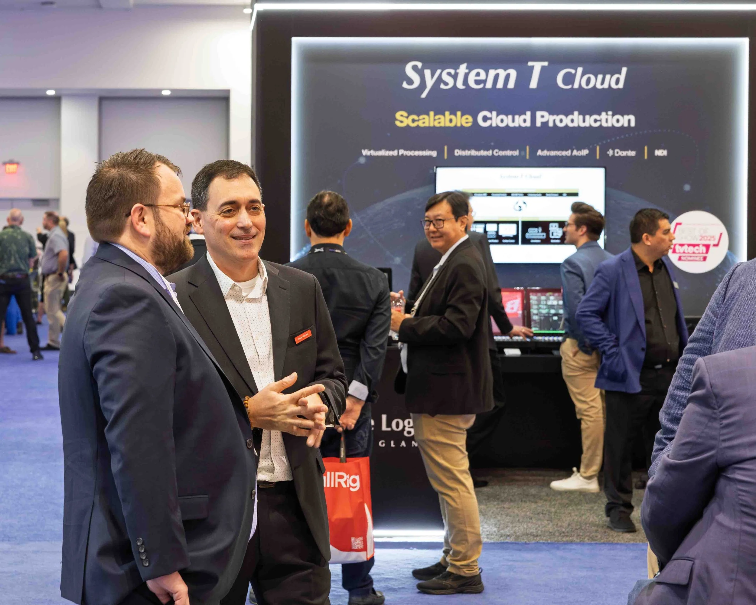 Business professionals engaging in conversations at a technology conference with a display board and monitors showcasing cloud technology.